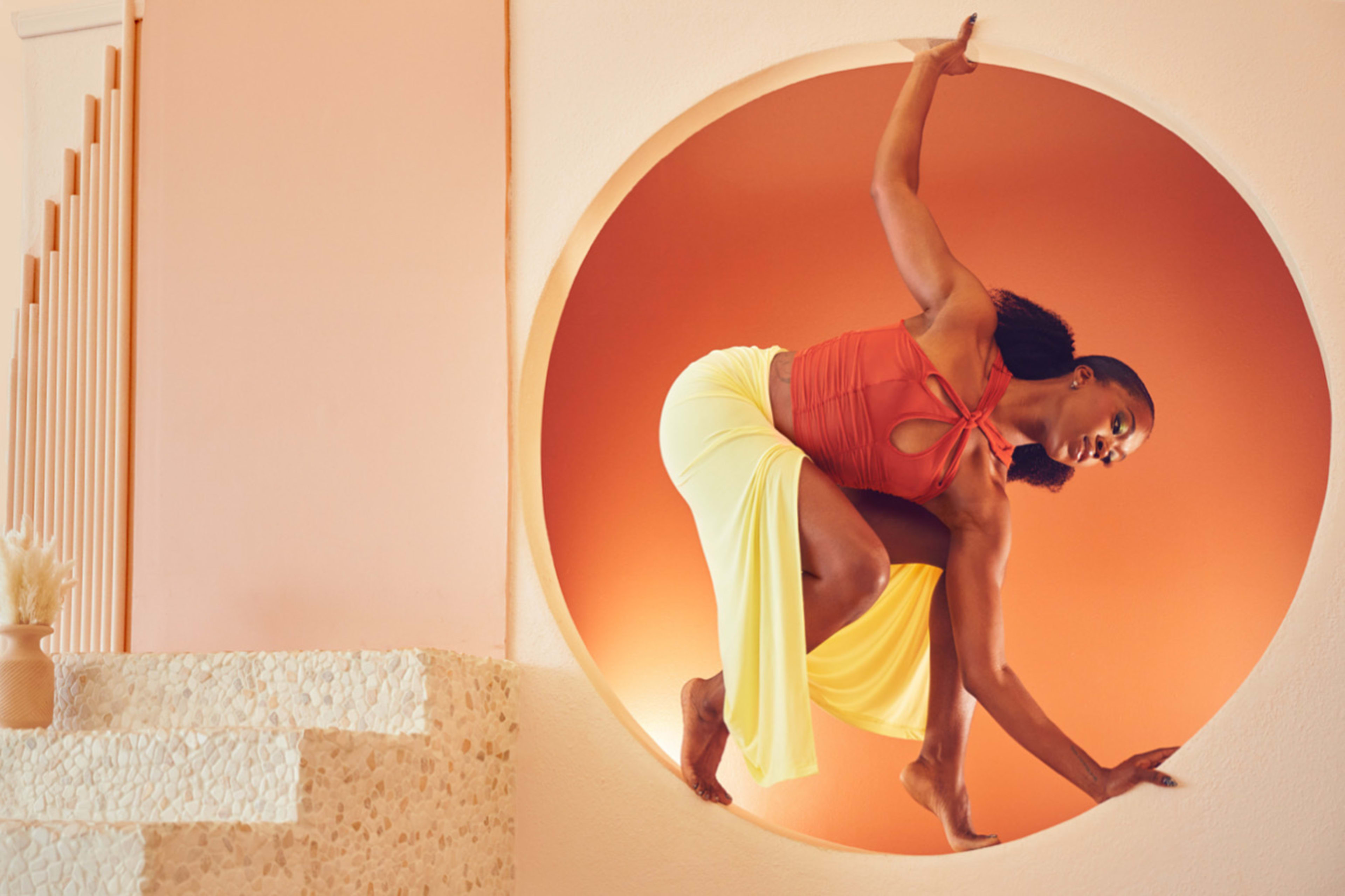 Eine Frau posiert während eines orange-beigen Fotoshootings in einem runden Fenster.