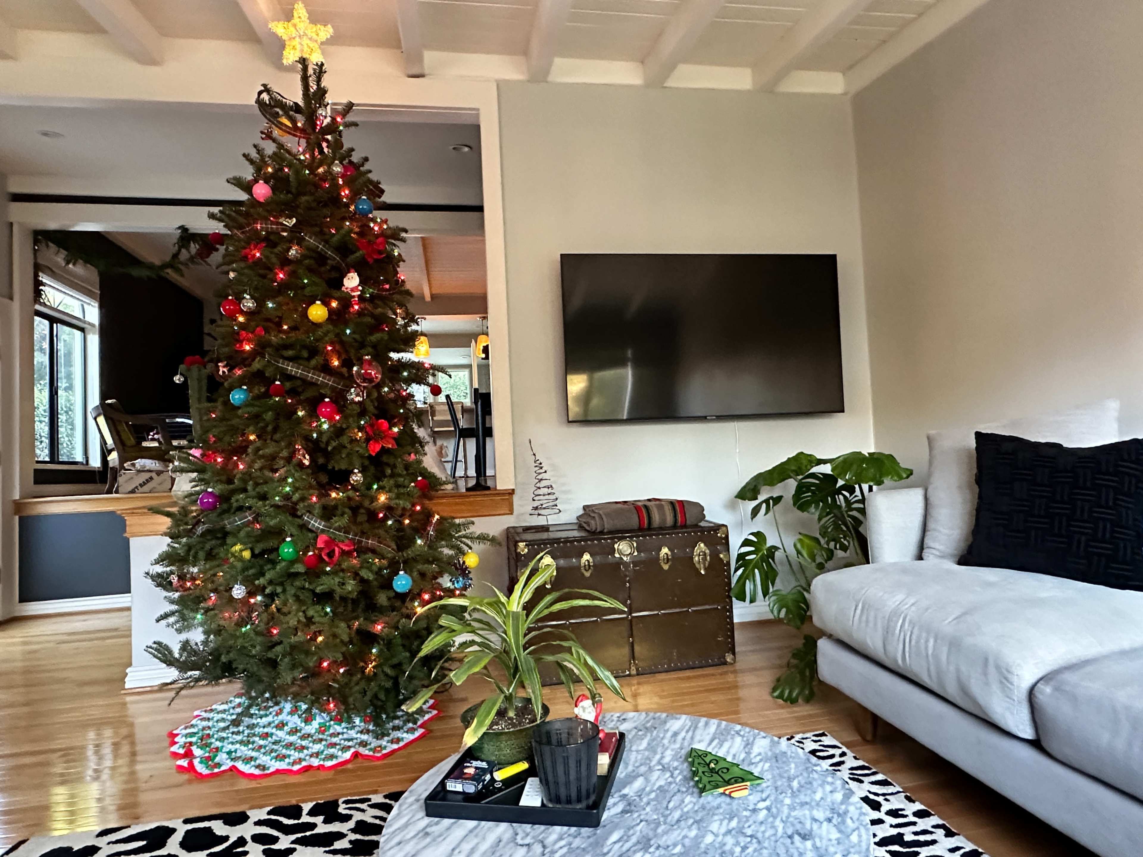 The image shows a living room with a decorated Christmas tree, a television mounted on the wall, a sofa, and a coffee table with a small plant.