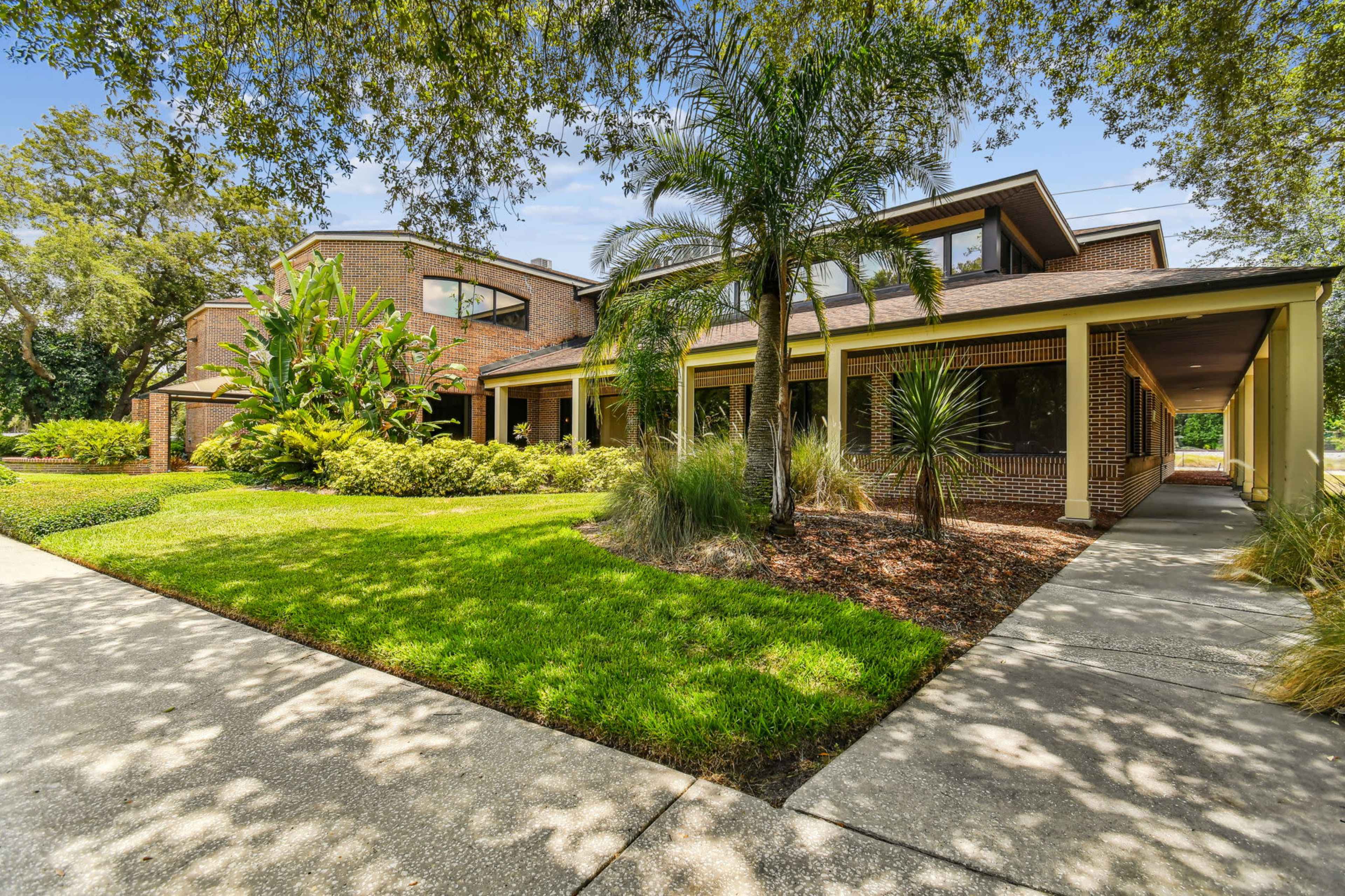 The image shows a two-story brick house with landscaped gardens and a paved walkway leading to an entrance.