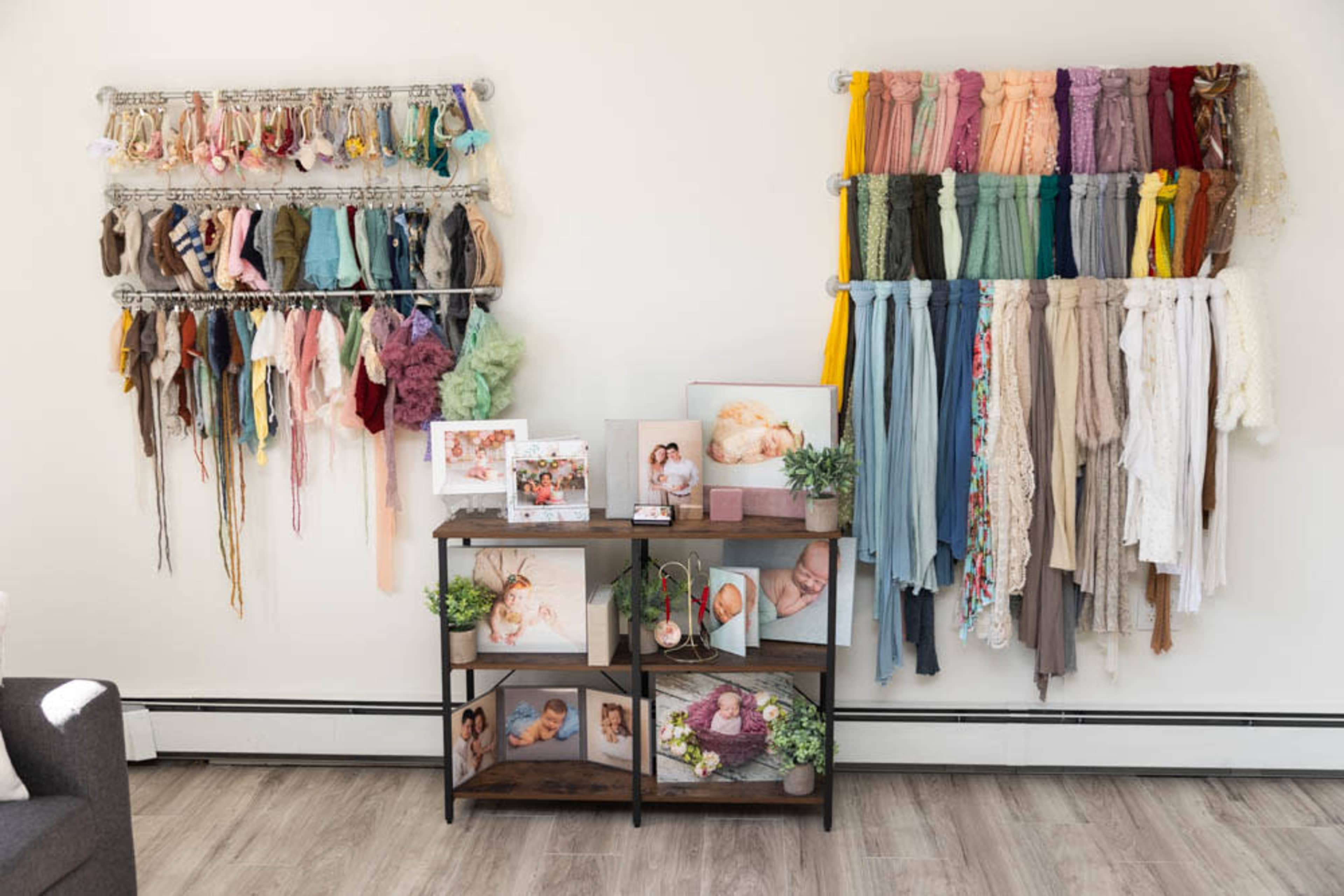 Two wall-mounted racks displaying various fabrics, alongside a wooden shelf with framed photos and decorative plants.