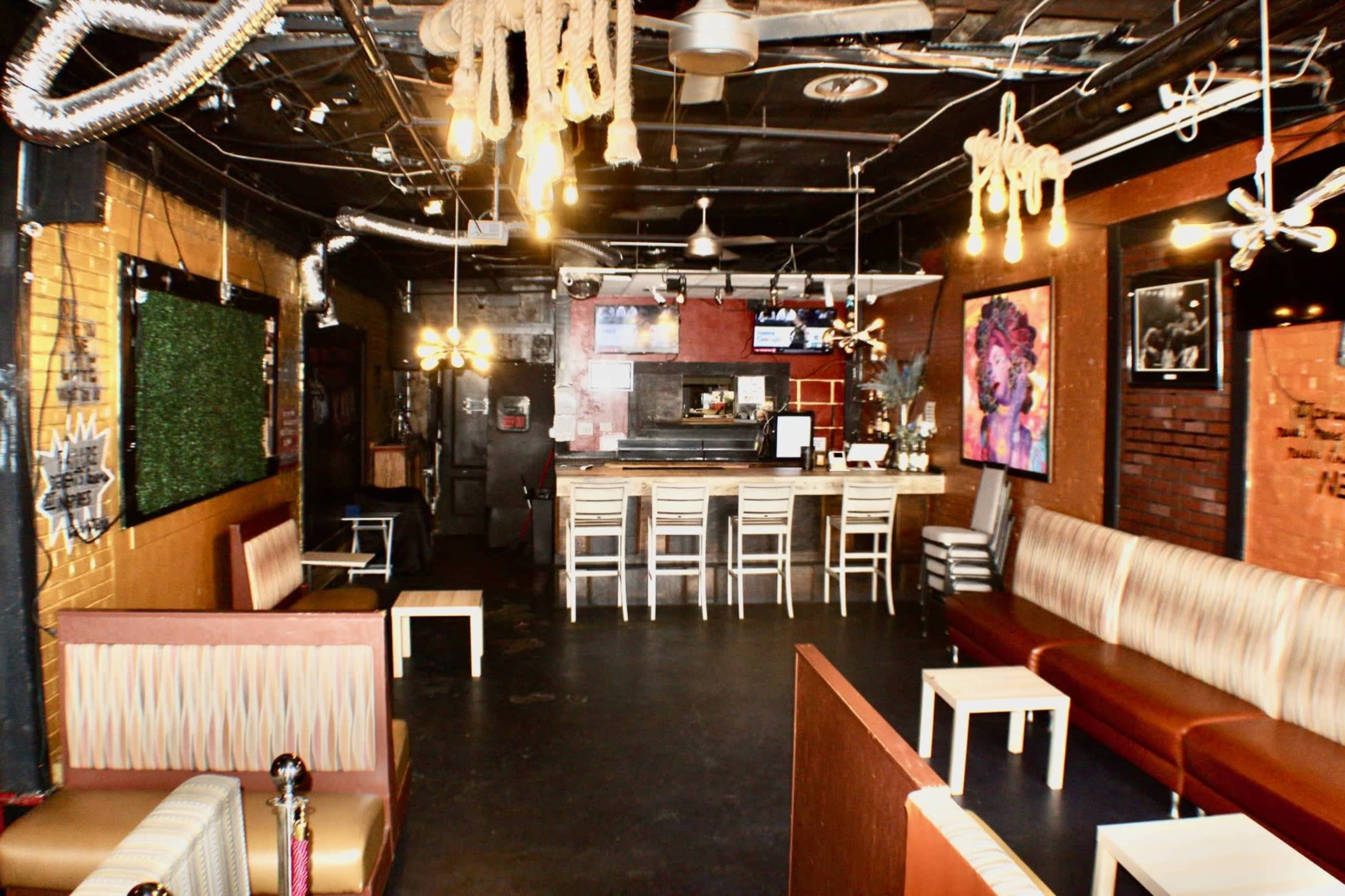The image shows a dimly lit bar interior with seating areas, a counter with stools, and decorative elements such as hanging lights and ropes.