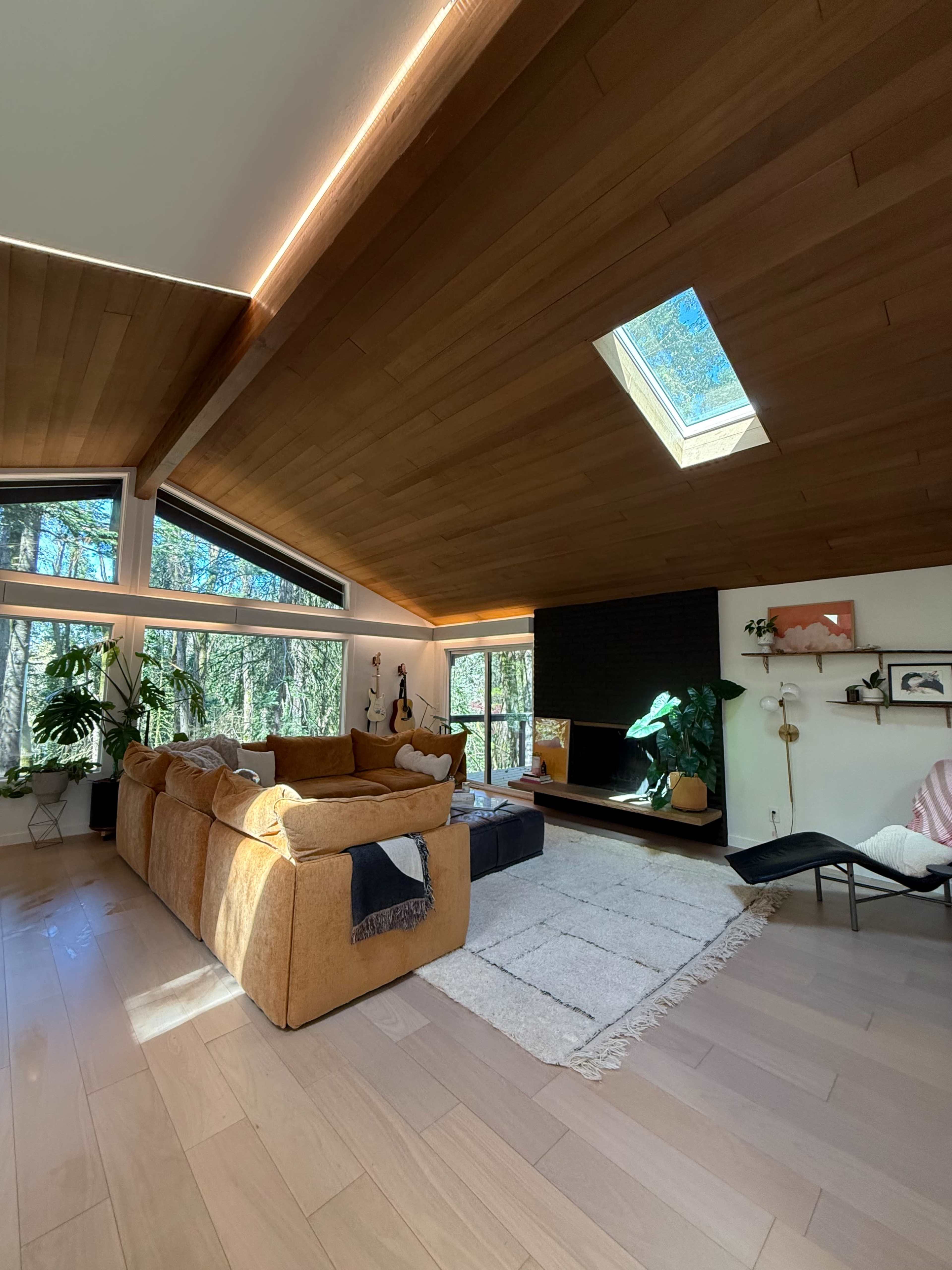 The image shows a modern living room with large windows, wooden ceilings, and a cozy couch positioned beside a light-colored area rug.