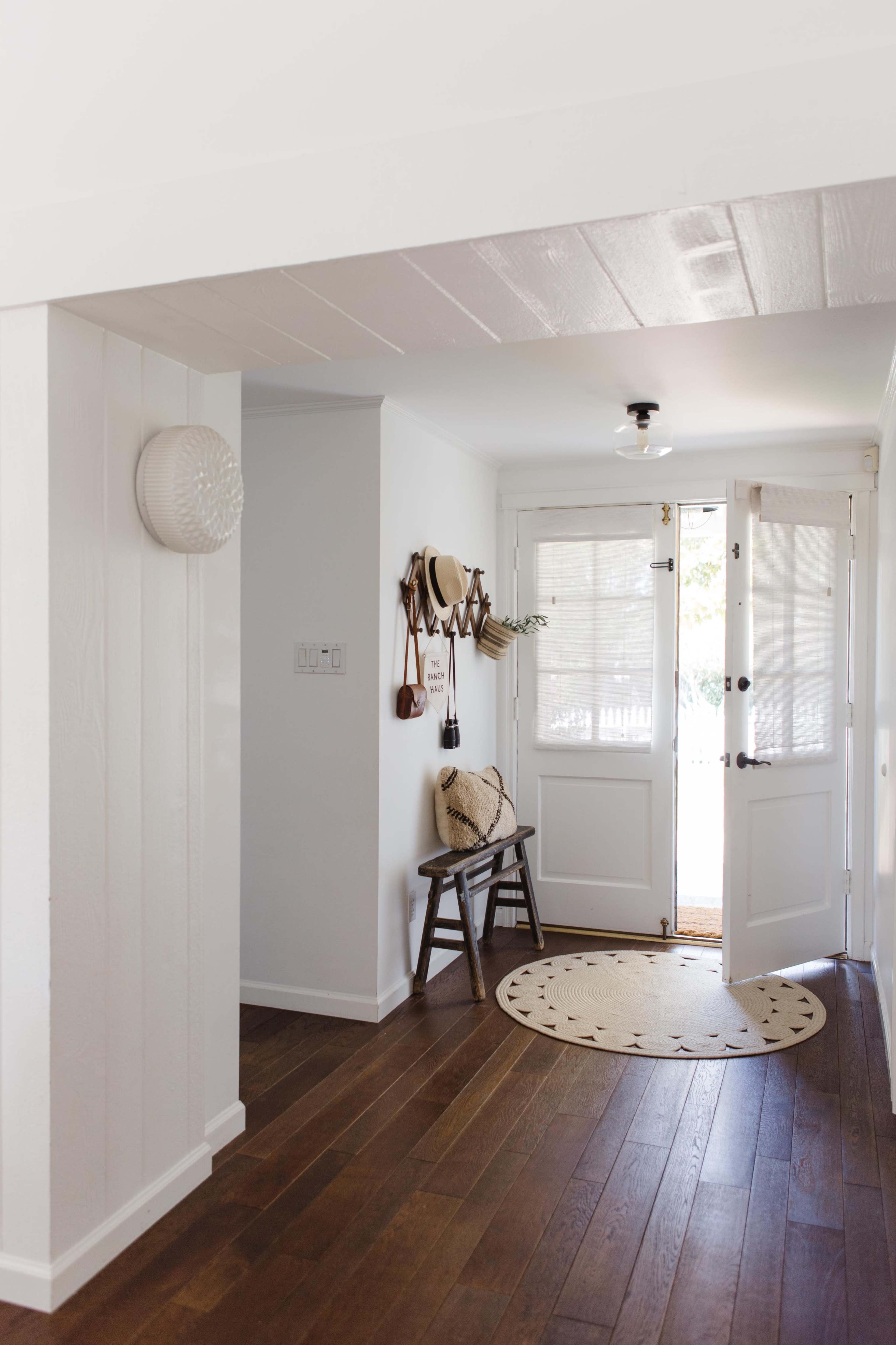 A bright entryway with a wooden bench, a round rug, and doors leading outside.