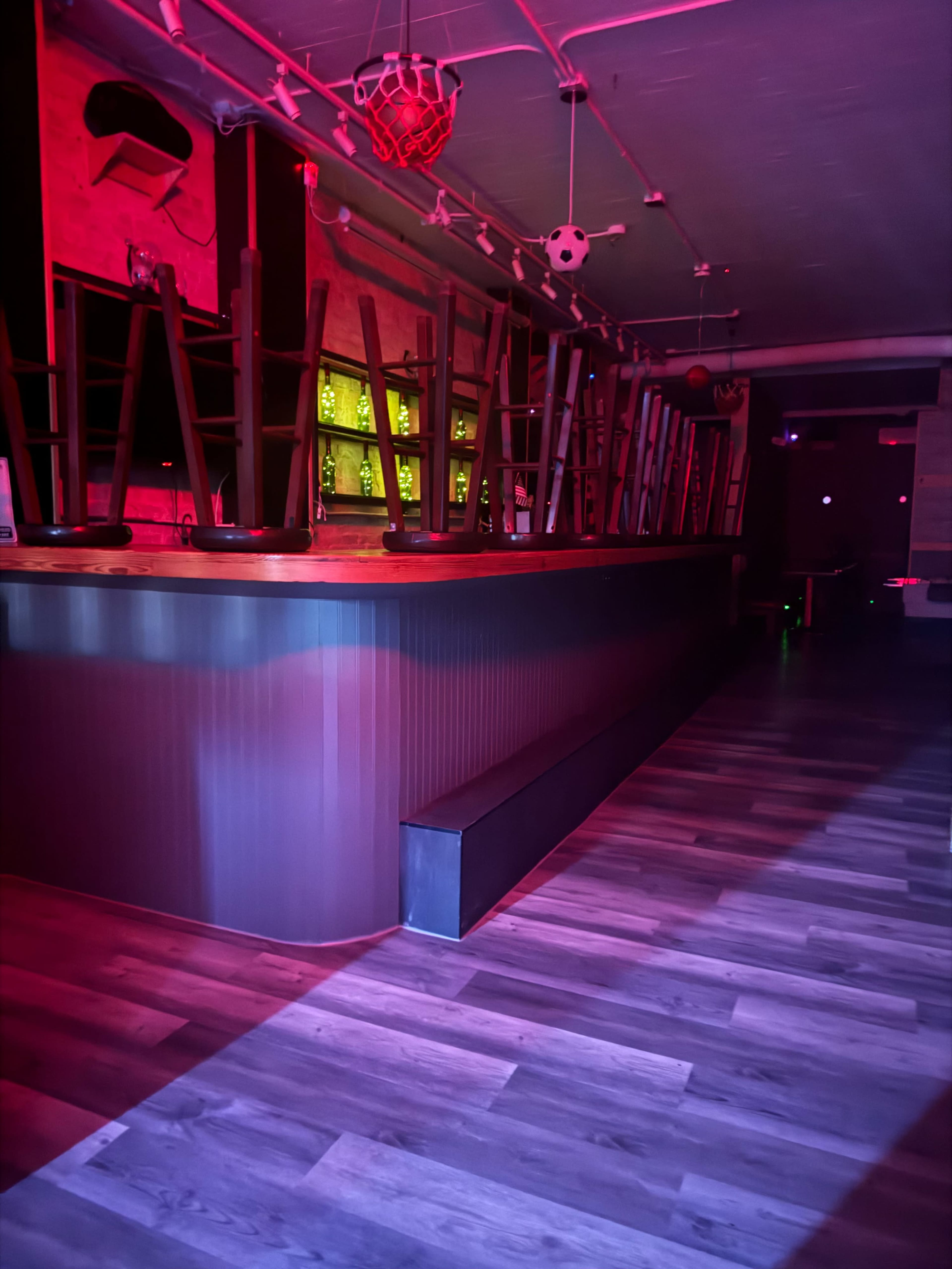 A dimly lit bar area with chairs stacked upside down on the counter and a wooden floor.