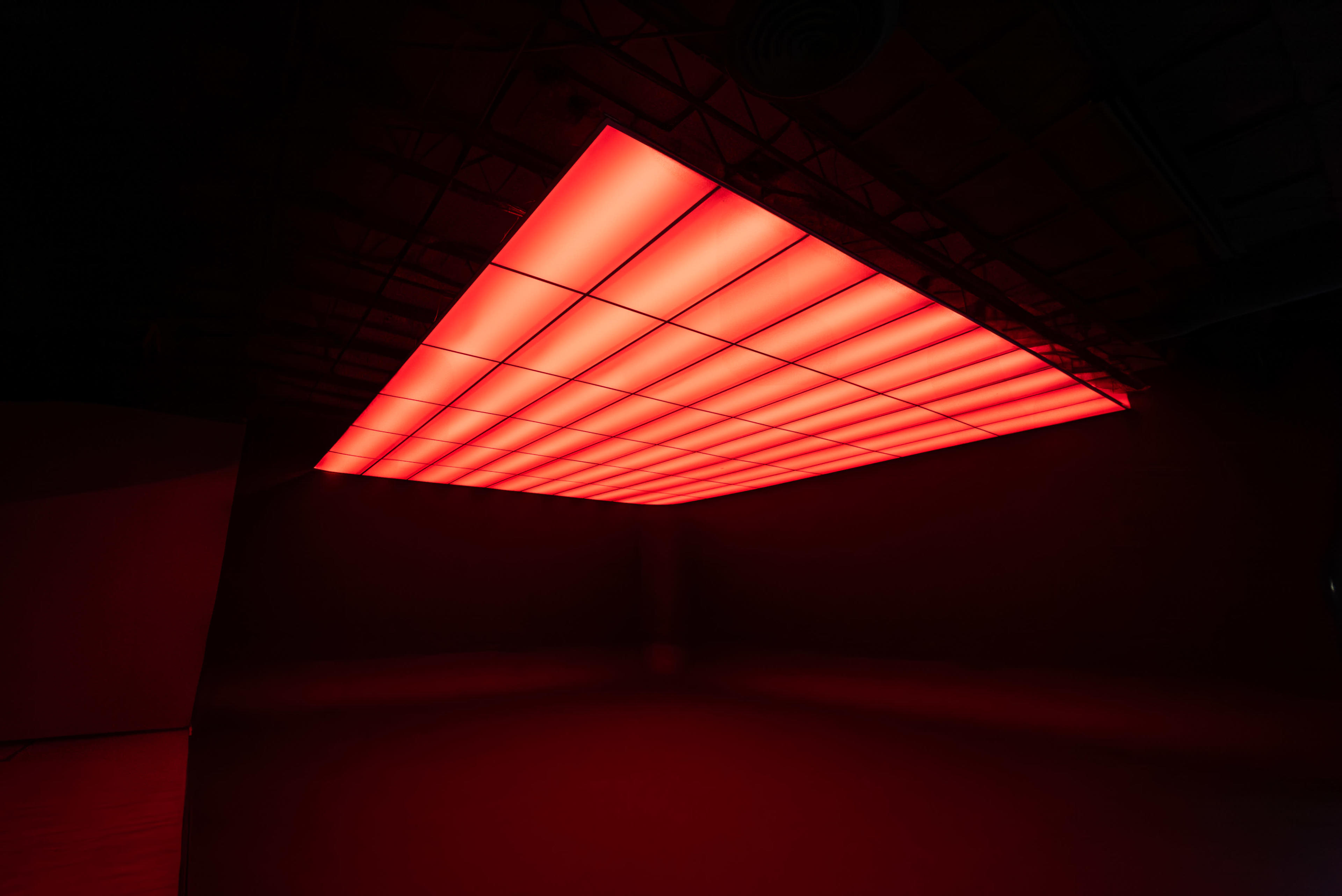 A large, rectangular panel of red lighting is suspended from the ceiling of an industrial space.