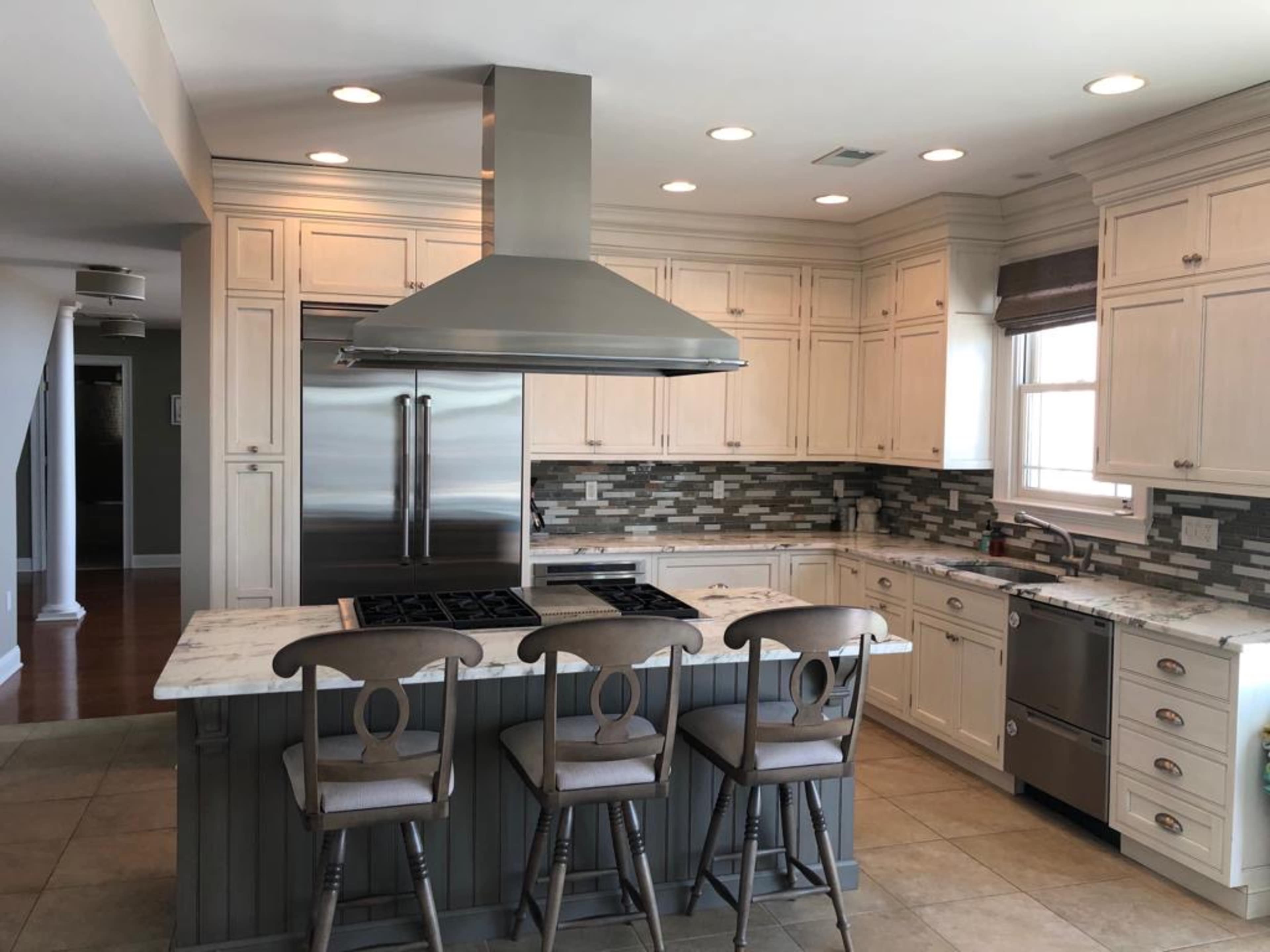 A modern kitchen featuring white cabinetry, a central island with bar stools, and stainless steel appliances.