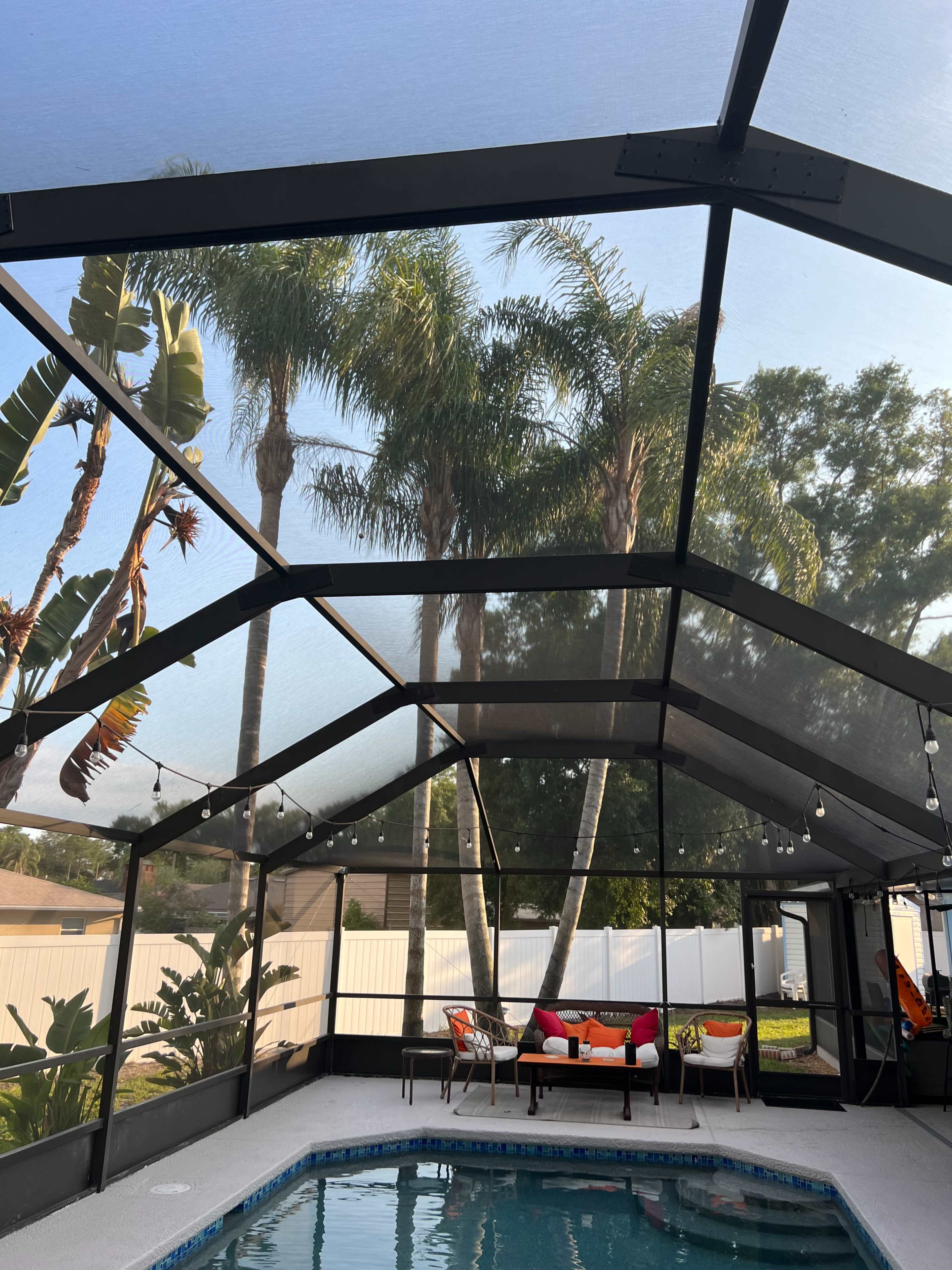 A screened-in patio with a swimming pool features seating arrangements and palm trees in the background.