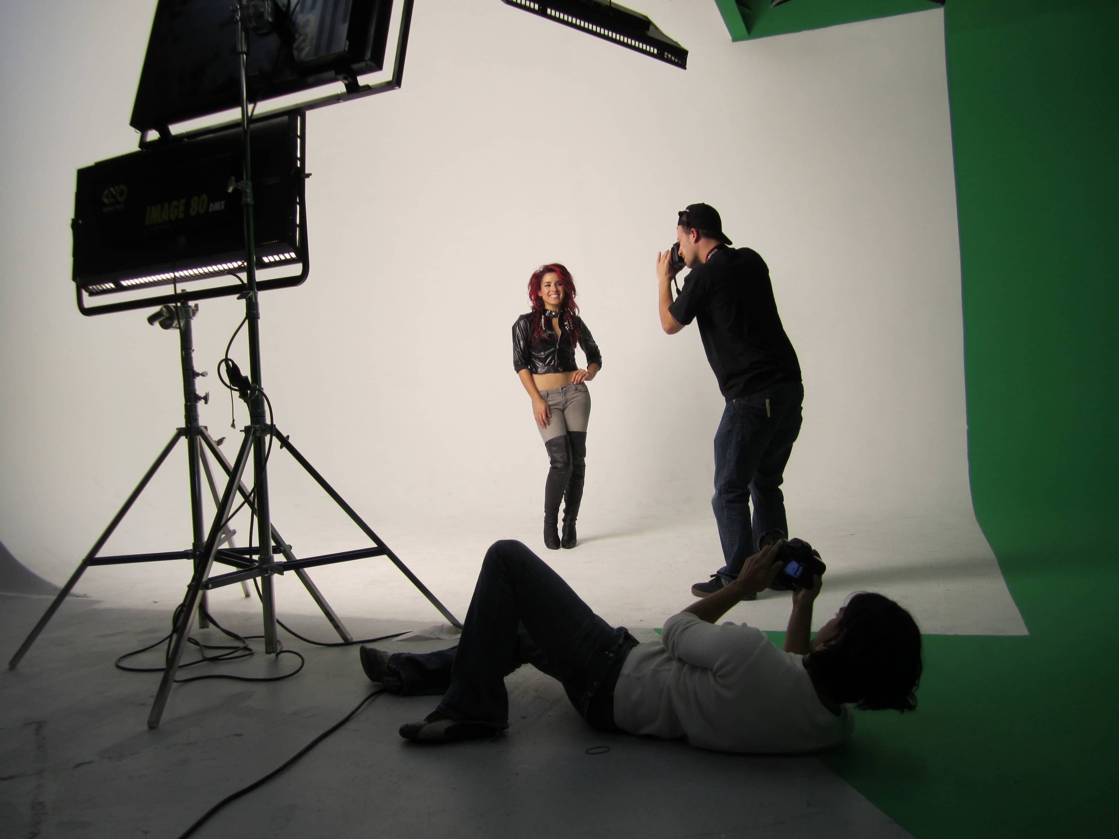 A model poses in front of a white backdrop while two photographers set up their shots.