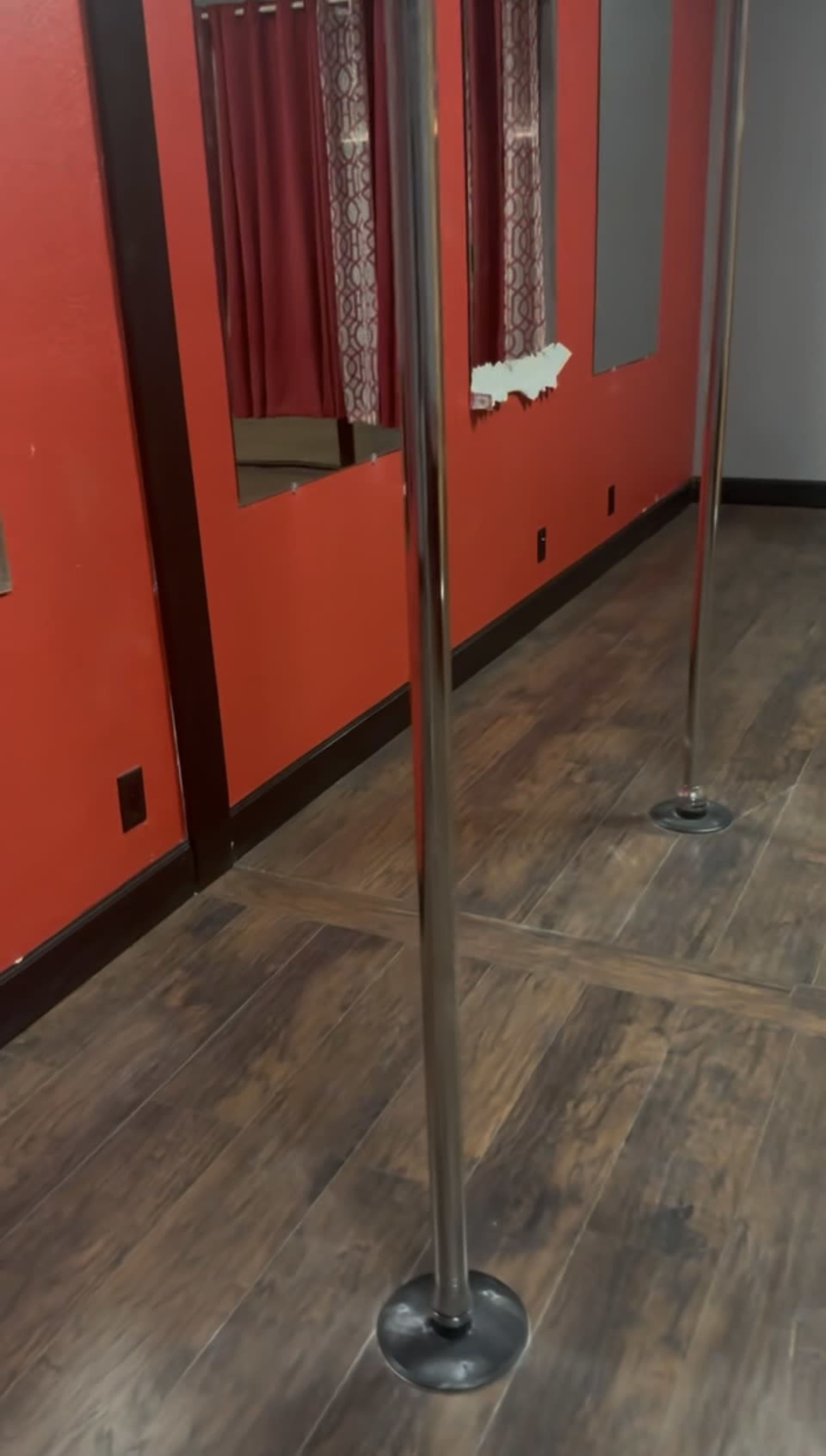 The image shows a room with red walls, a wooden floor, and two metallic poles set on black bases.
