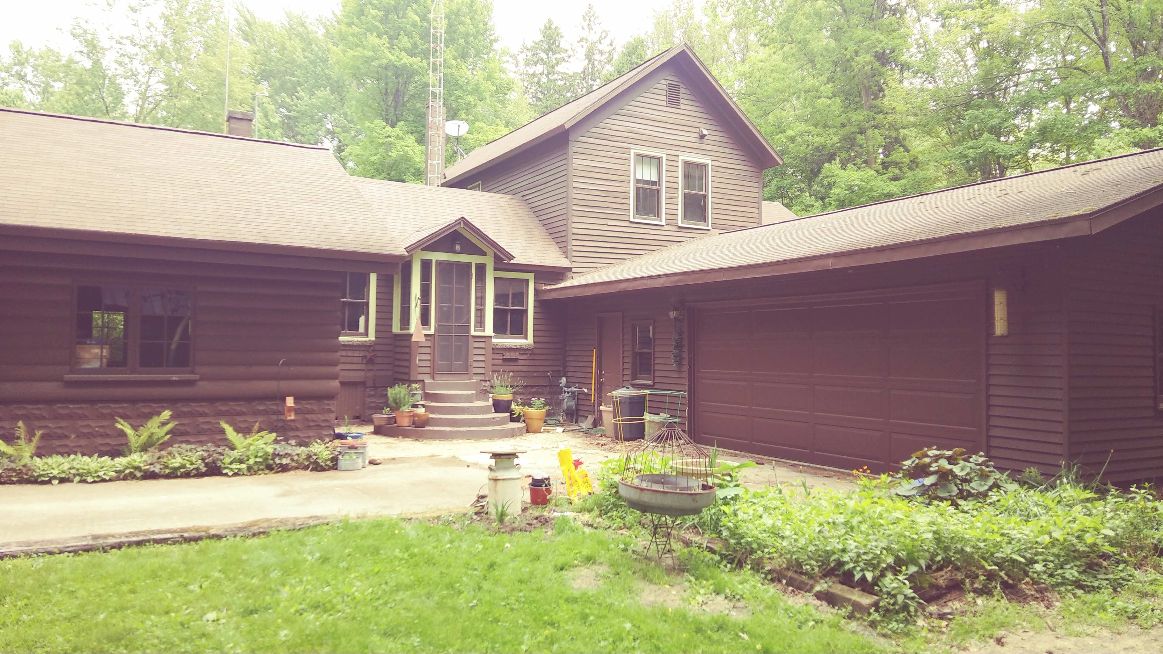 A two-story brown wooden house with a porch, a garage, and a landscaped yard.