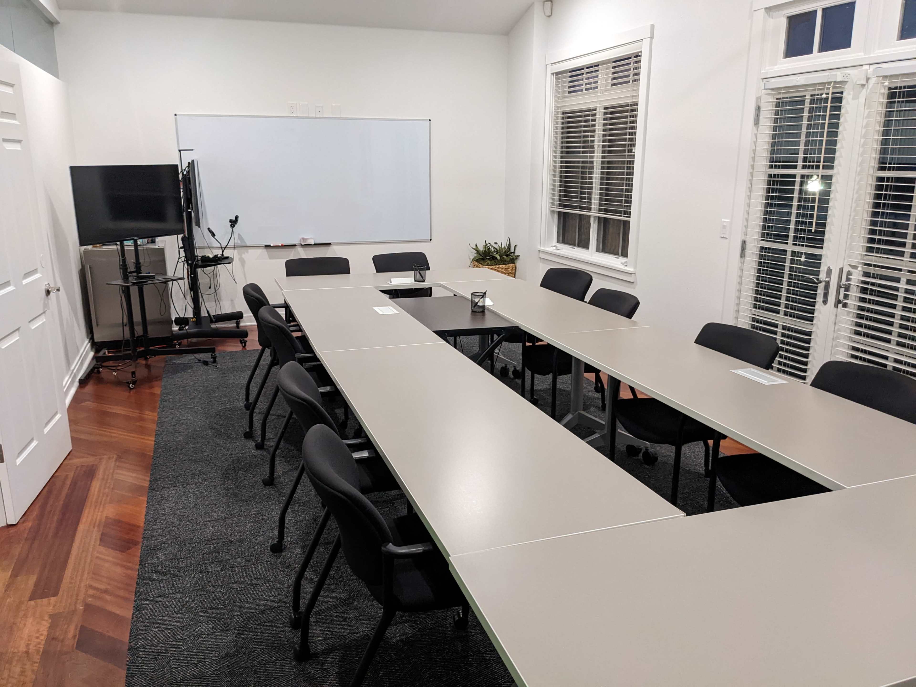 A conference room with a long rectangular table surrounded by chairs and a whiteboard at the front.