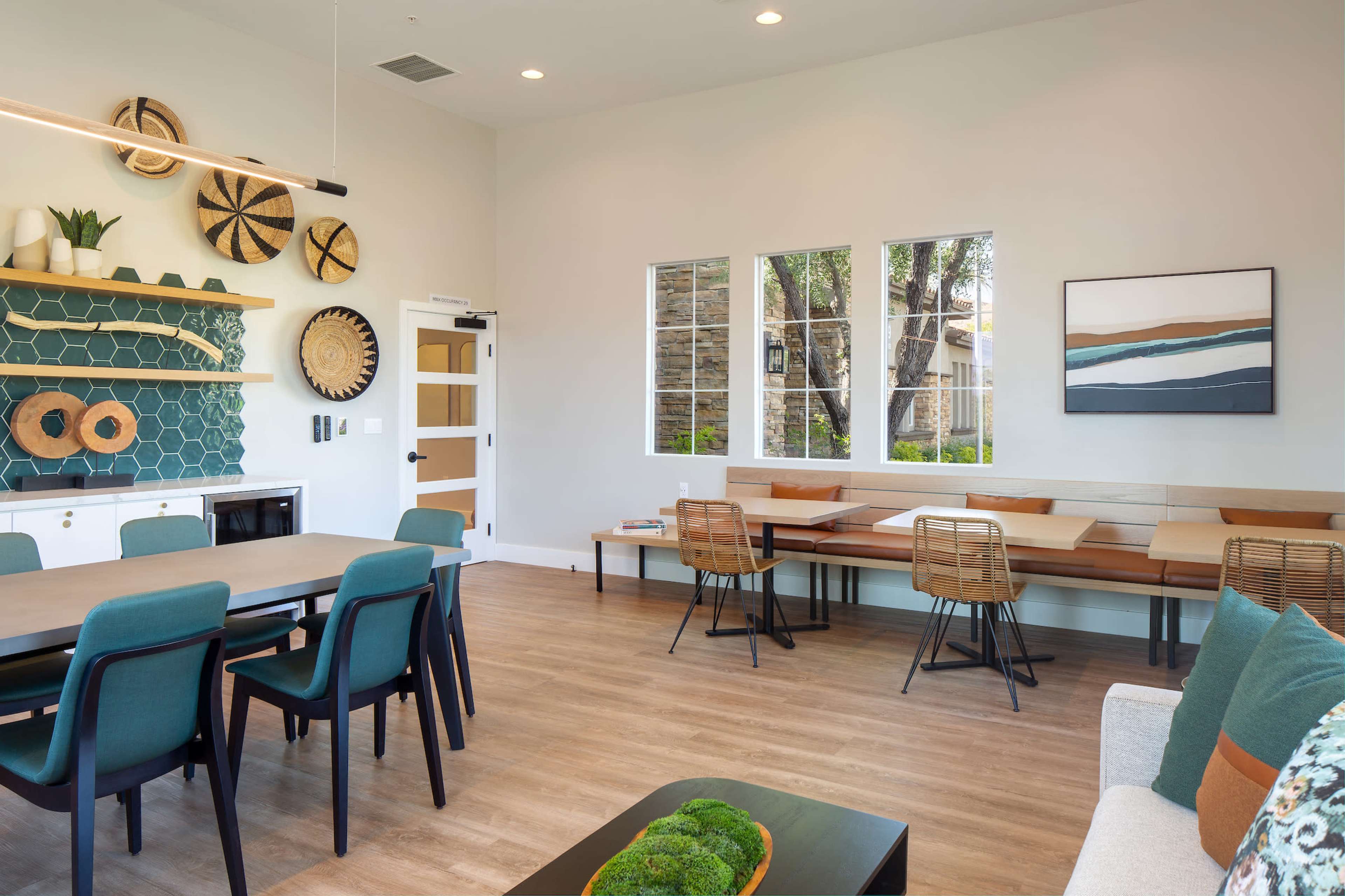 A modern indoor communal space featuring a dining area with a long table, various seating arrangements, and decorative wall elements.