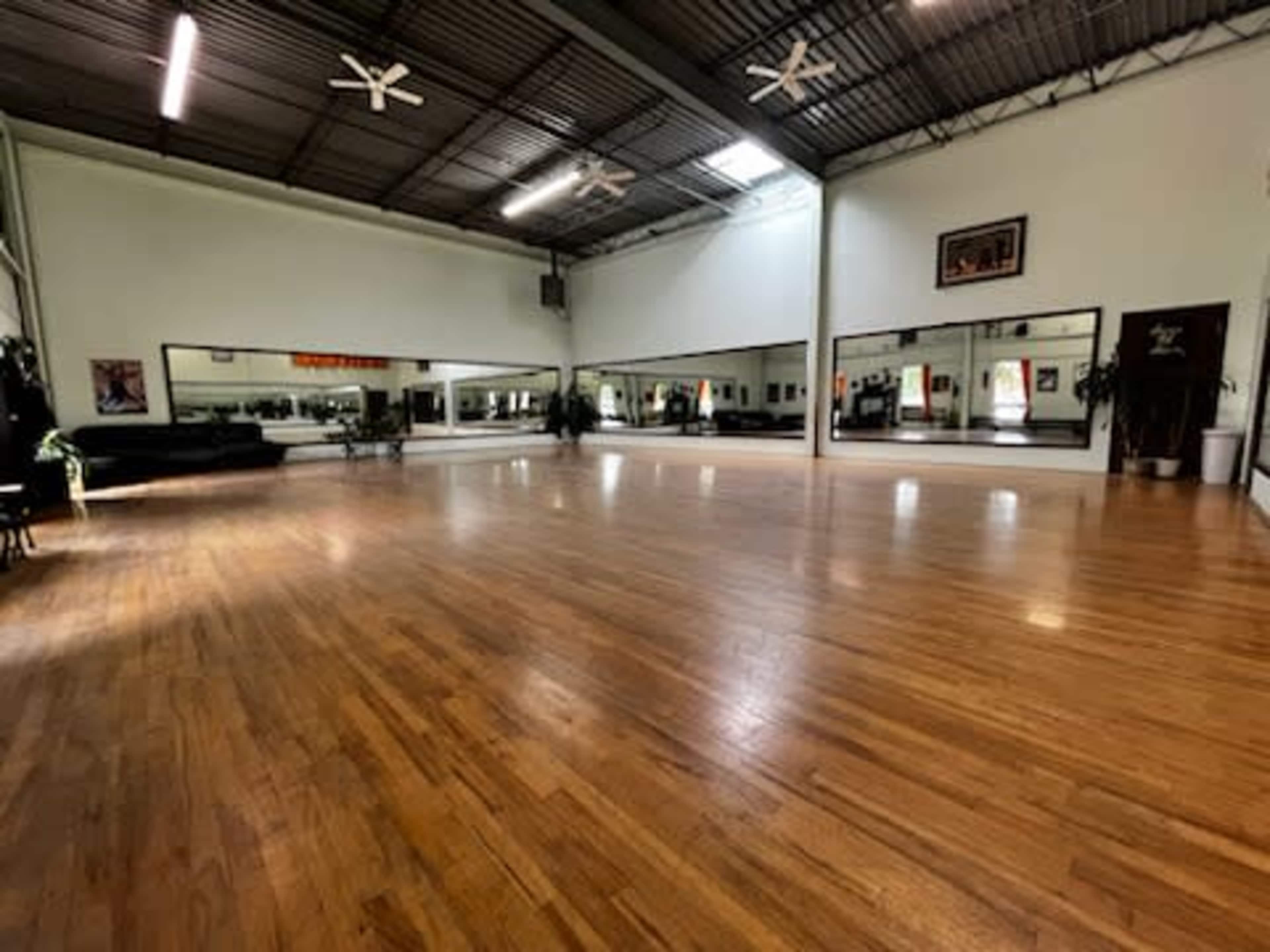 A spacious wooden dance studio with mirrors lining the walls and large windows allowing natural light to enter.