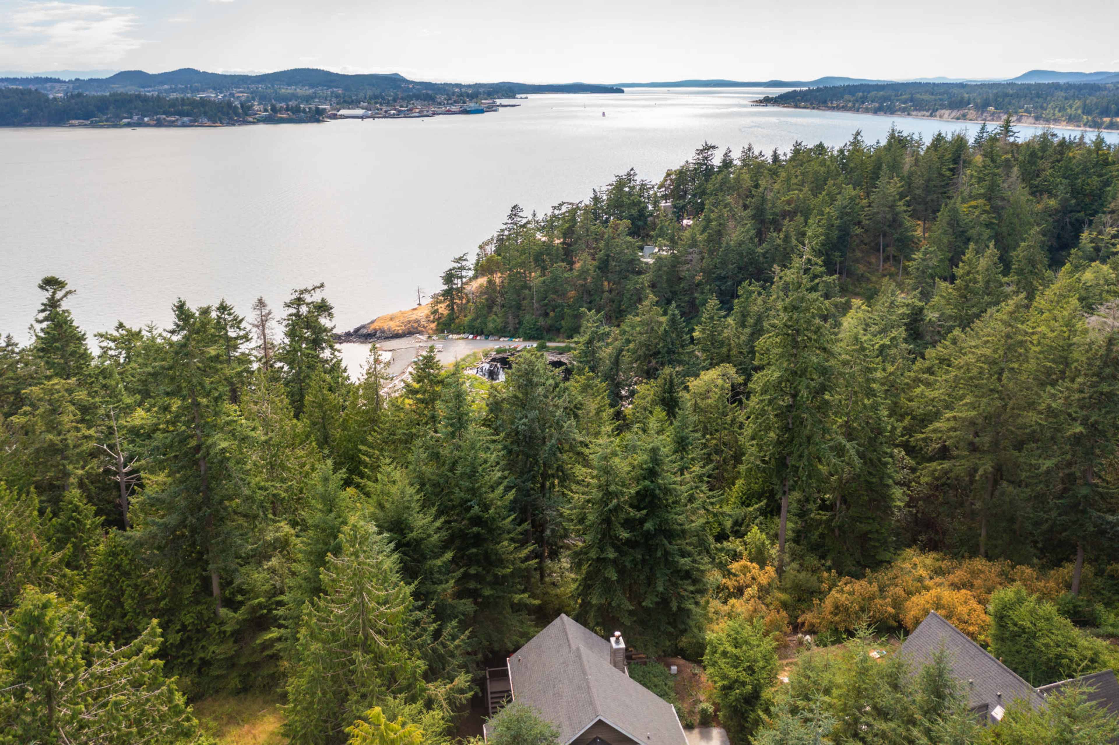 A coastal landscape with a view of a river or bay, surrounded by dense trees and residential homes in the foreground.
