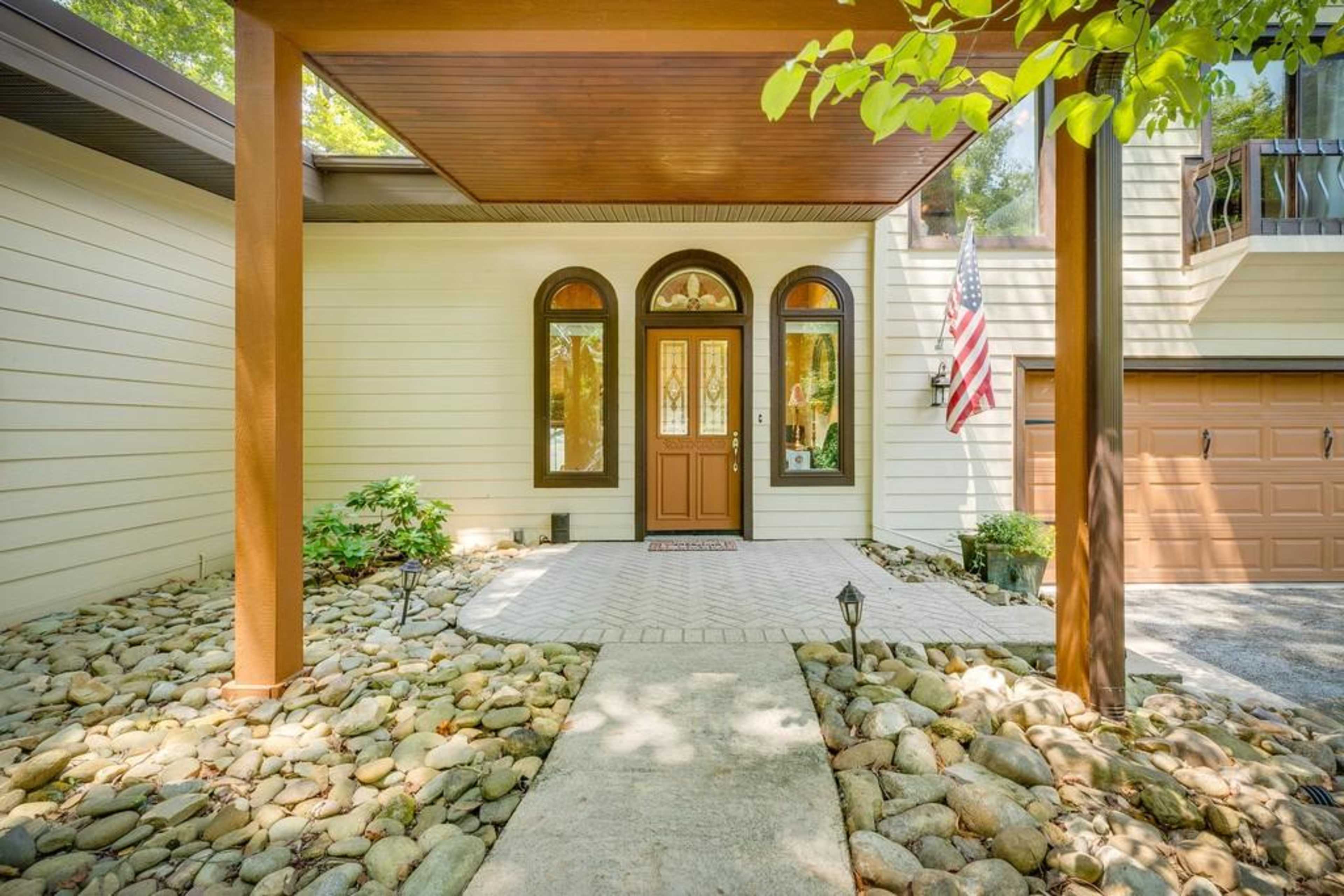 The entrance of a house with a stone pathway leading to a door under a covered porch and an American flag displayed.