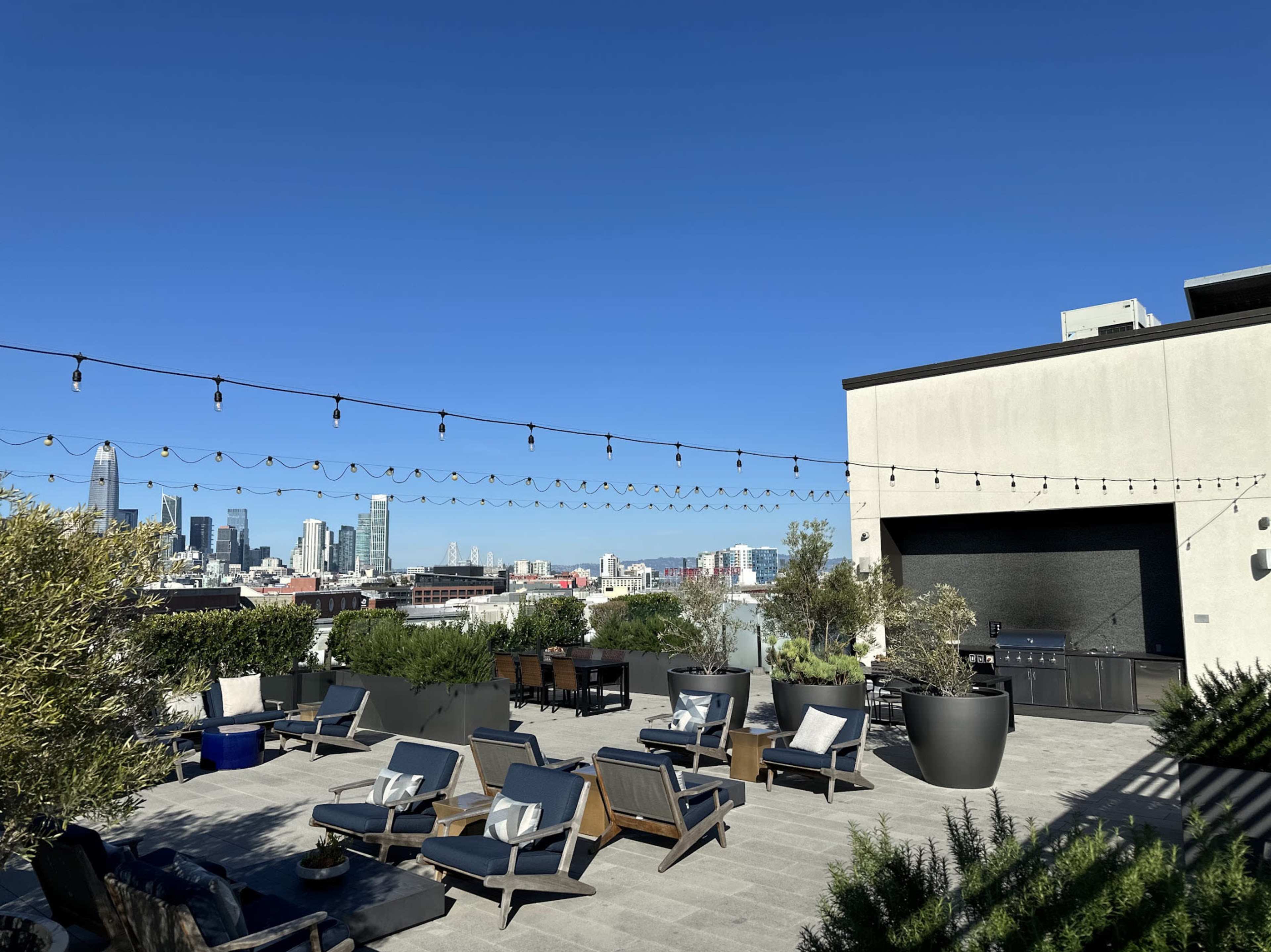 A rooftop terrace features outdoor seating and string lights with a city skyline in the background.