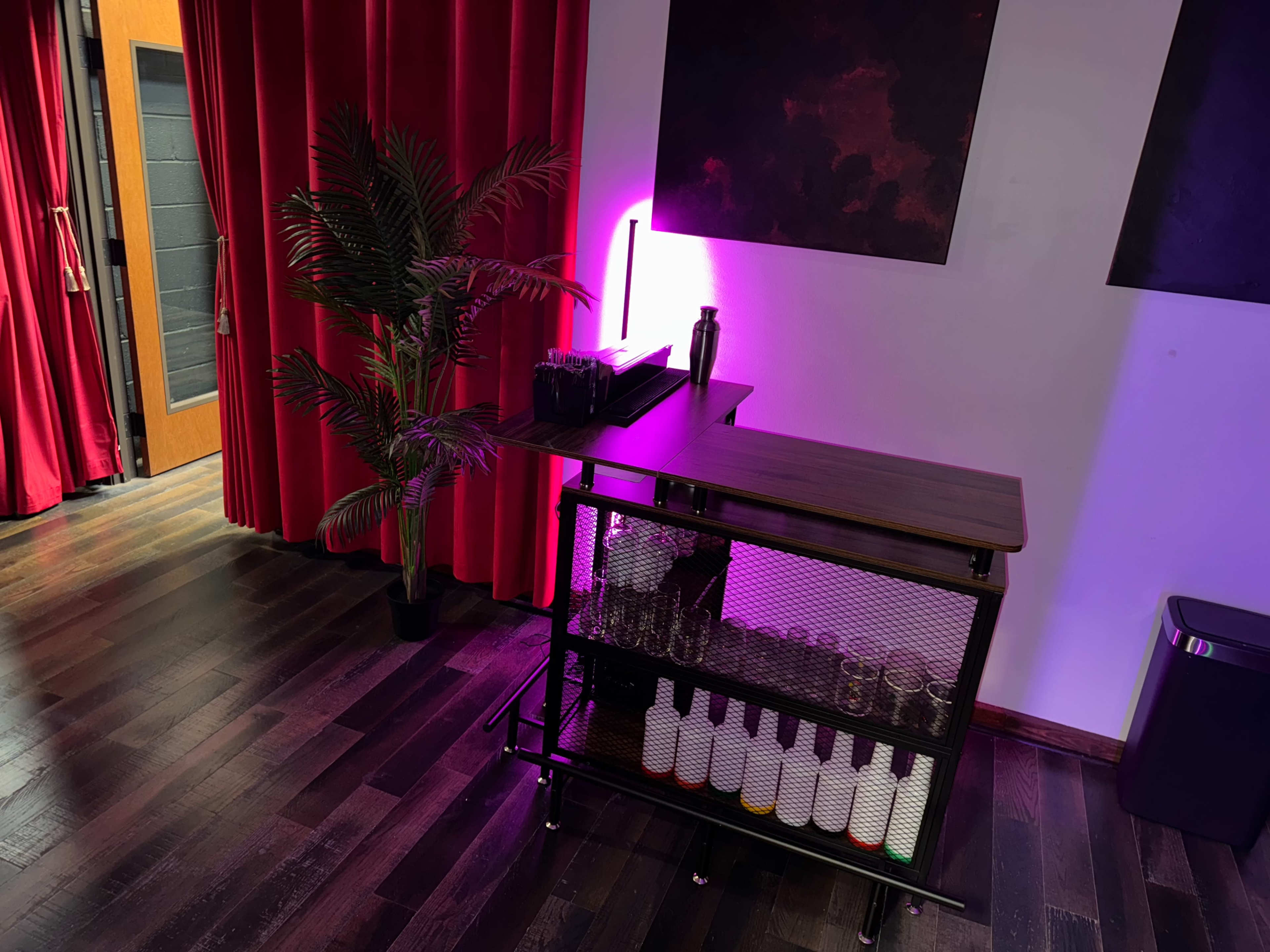 The image shows a stylish bar cart with various bottles and a glowing light, set against a backdrop of red curtains and a dark wall.