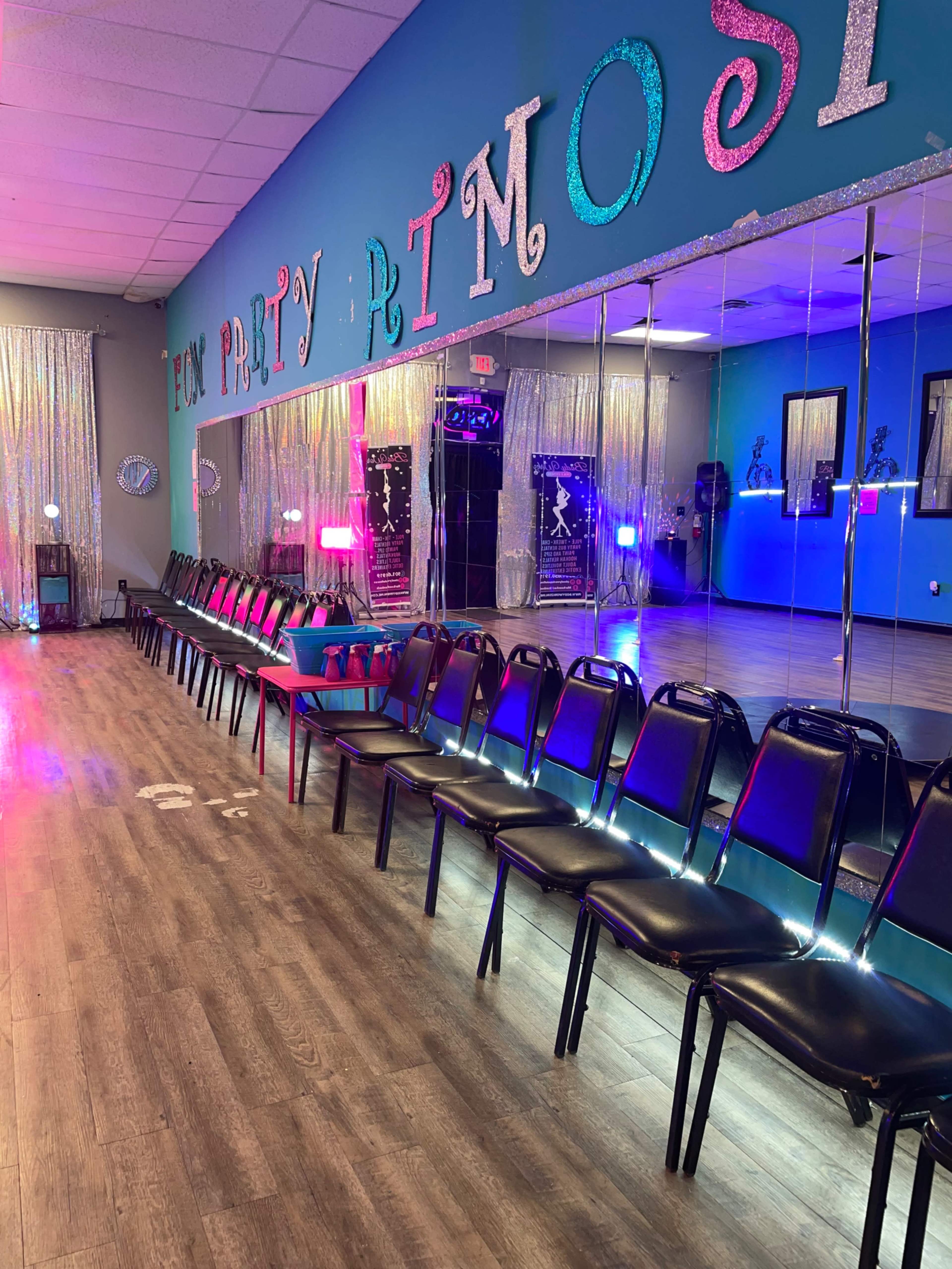 A row of black chairs is positioned along a wall with a large mirror and colorful decorations in a brightly lit party room.