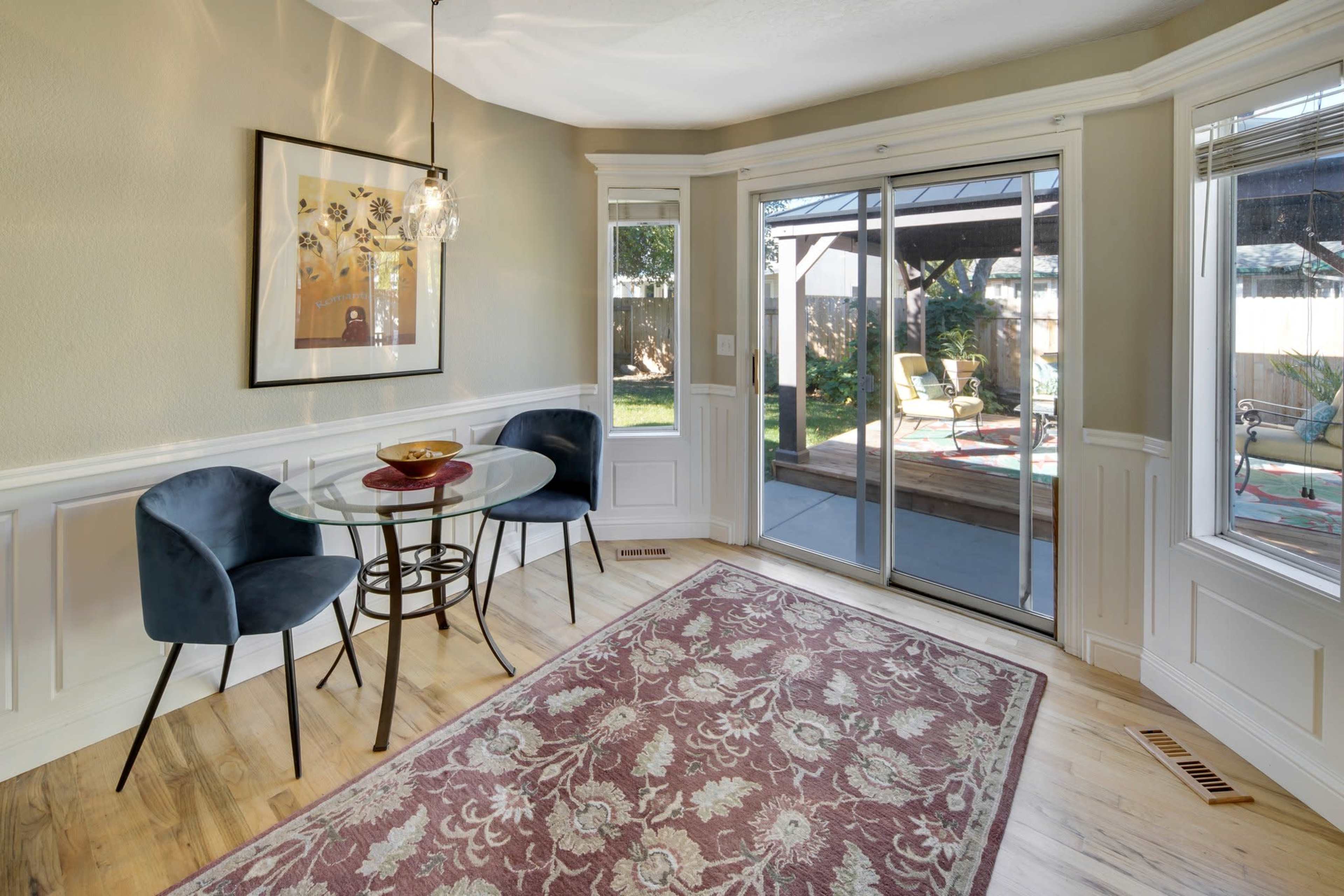 A small dining area features a round table with two chairs, a decorative rug, and glass doors leading to an outdoor patio.