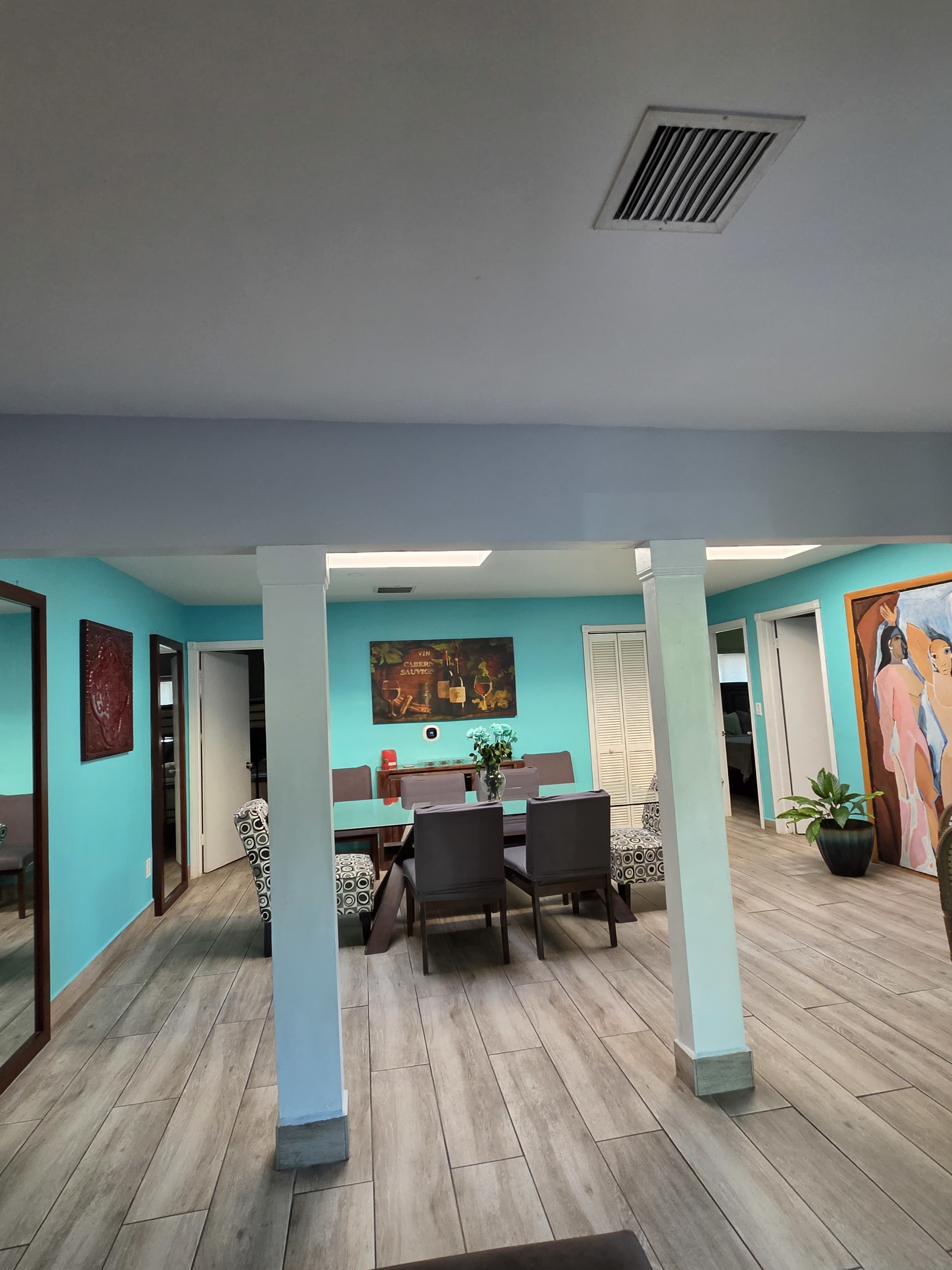 The image shows a brightly colored room with turquoise walls, a dining table set for six, and art pieces on the walls.
