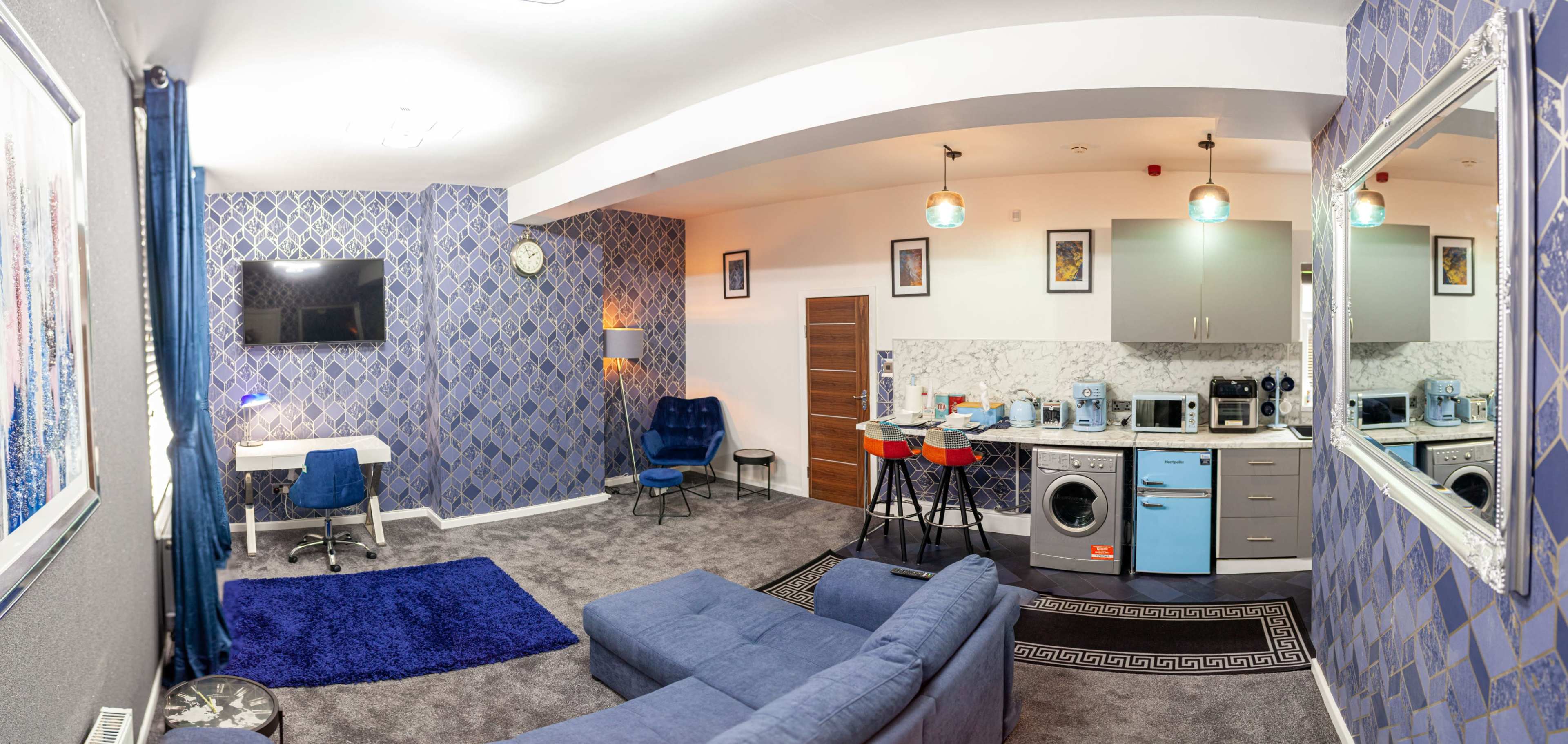 A modern studio apartment with a living area, kitchen, and workspace, featuring blue accents and contemporary furnishings.