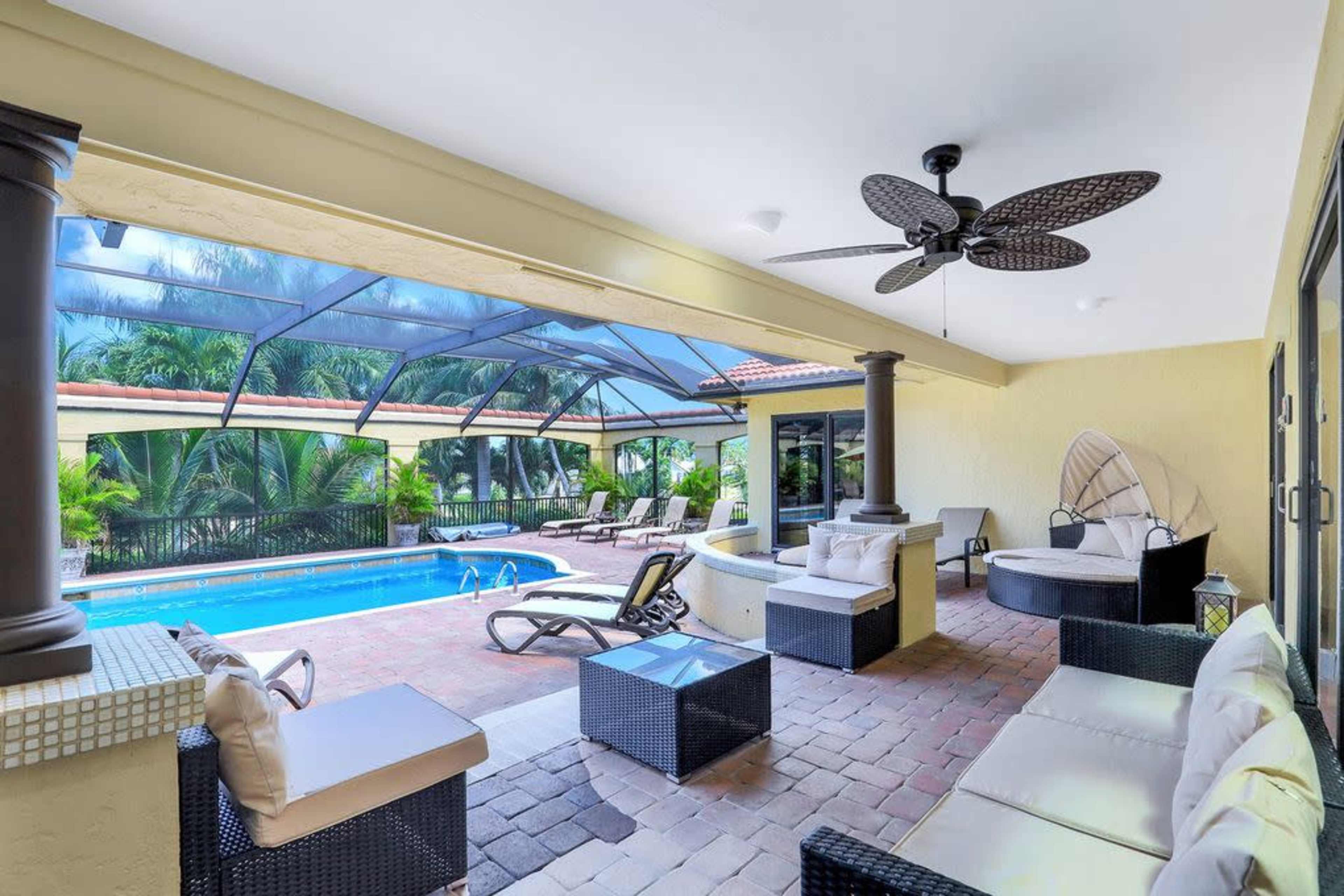 A covered outdoor patio with wicker furniture overlooking a swimming pool enclosed by a screen.