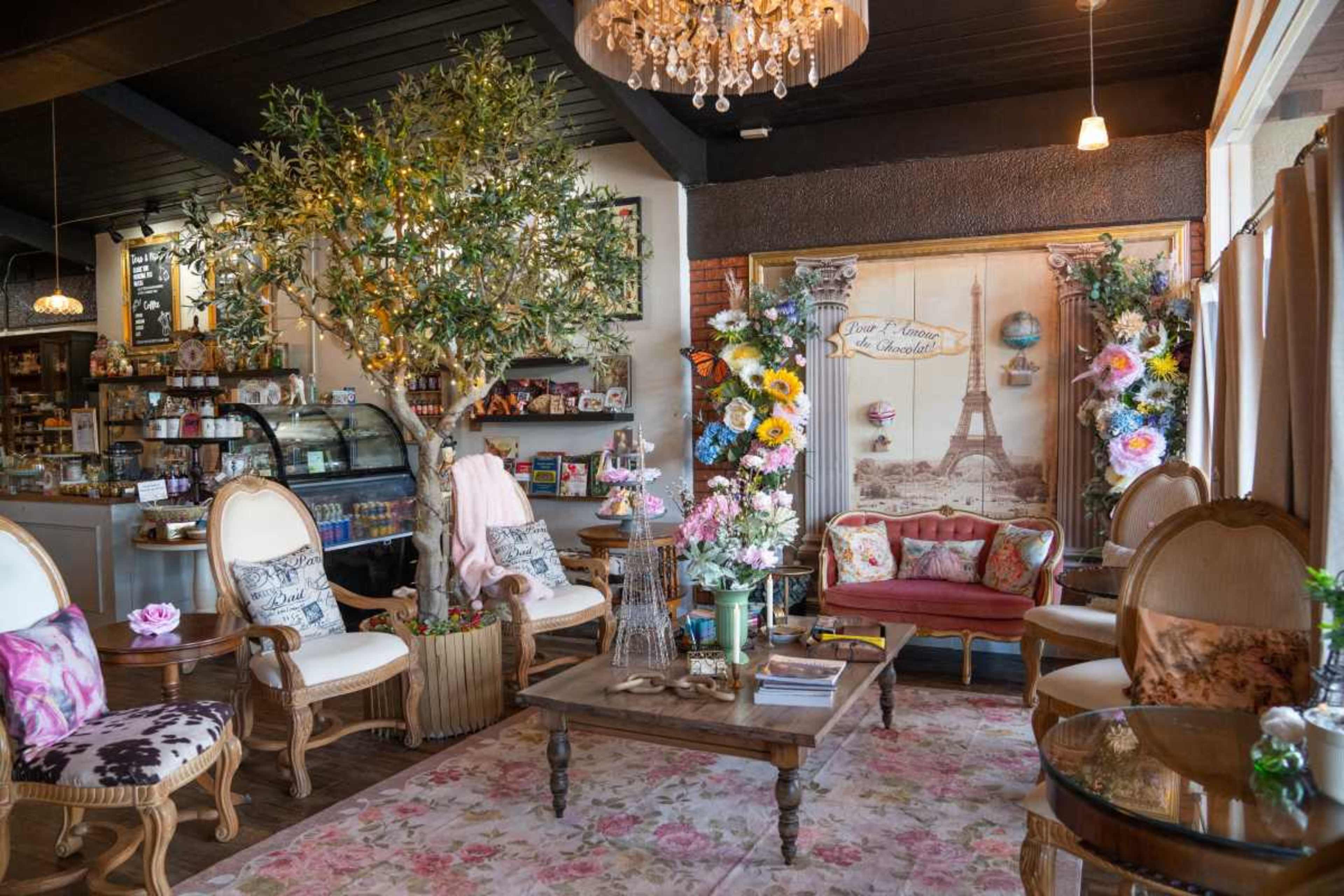 The image depicts a cozy cafe interior with ornate seating, floral decorations, and a decorative wall mural featuring the Eiffel Tower.