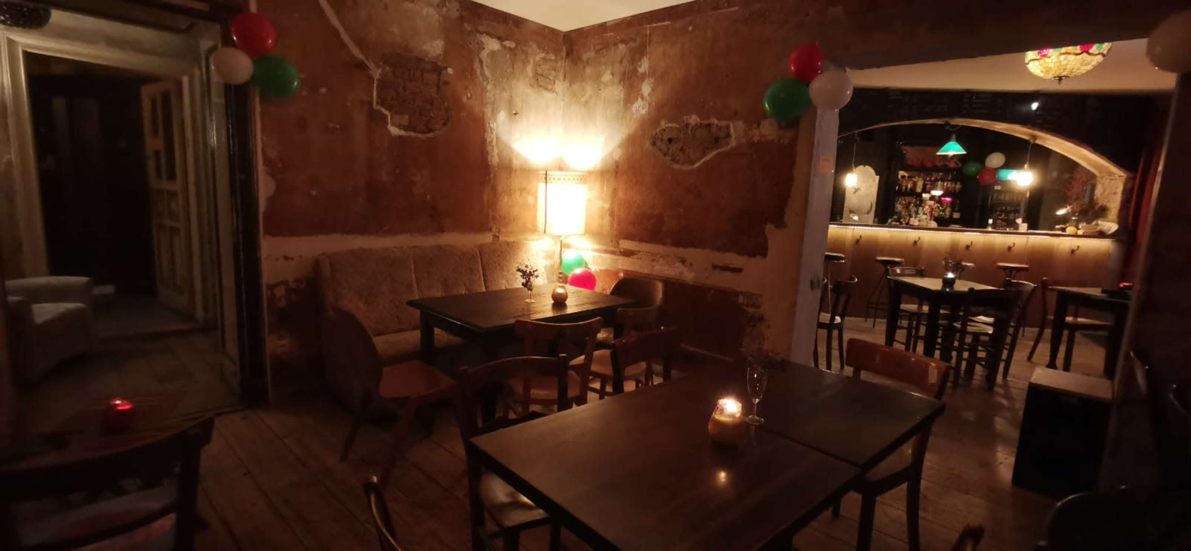 The image shows a dimly lit bar interior with exposed walls, wooden tables, and balloons in the decor.