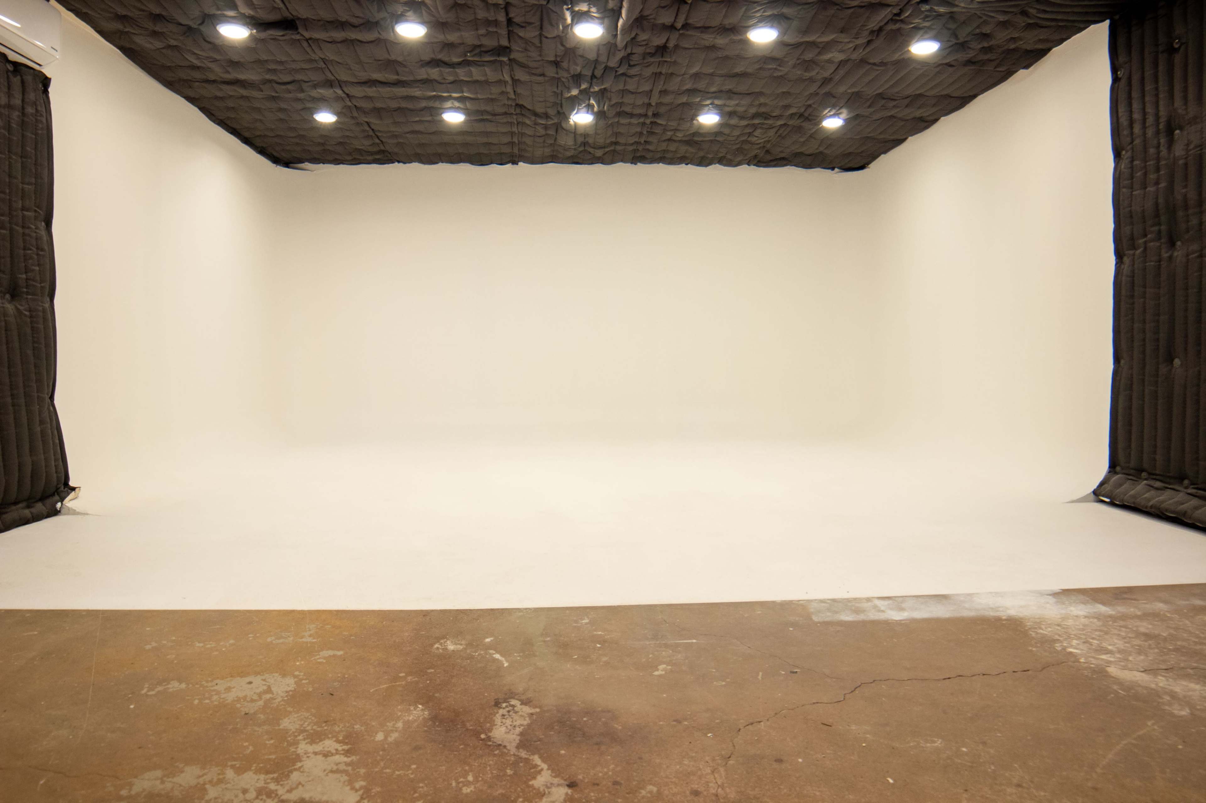 The image shows a large, empty studio space with a smooth white backdrop and padded black walls.