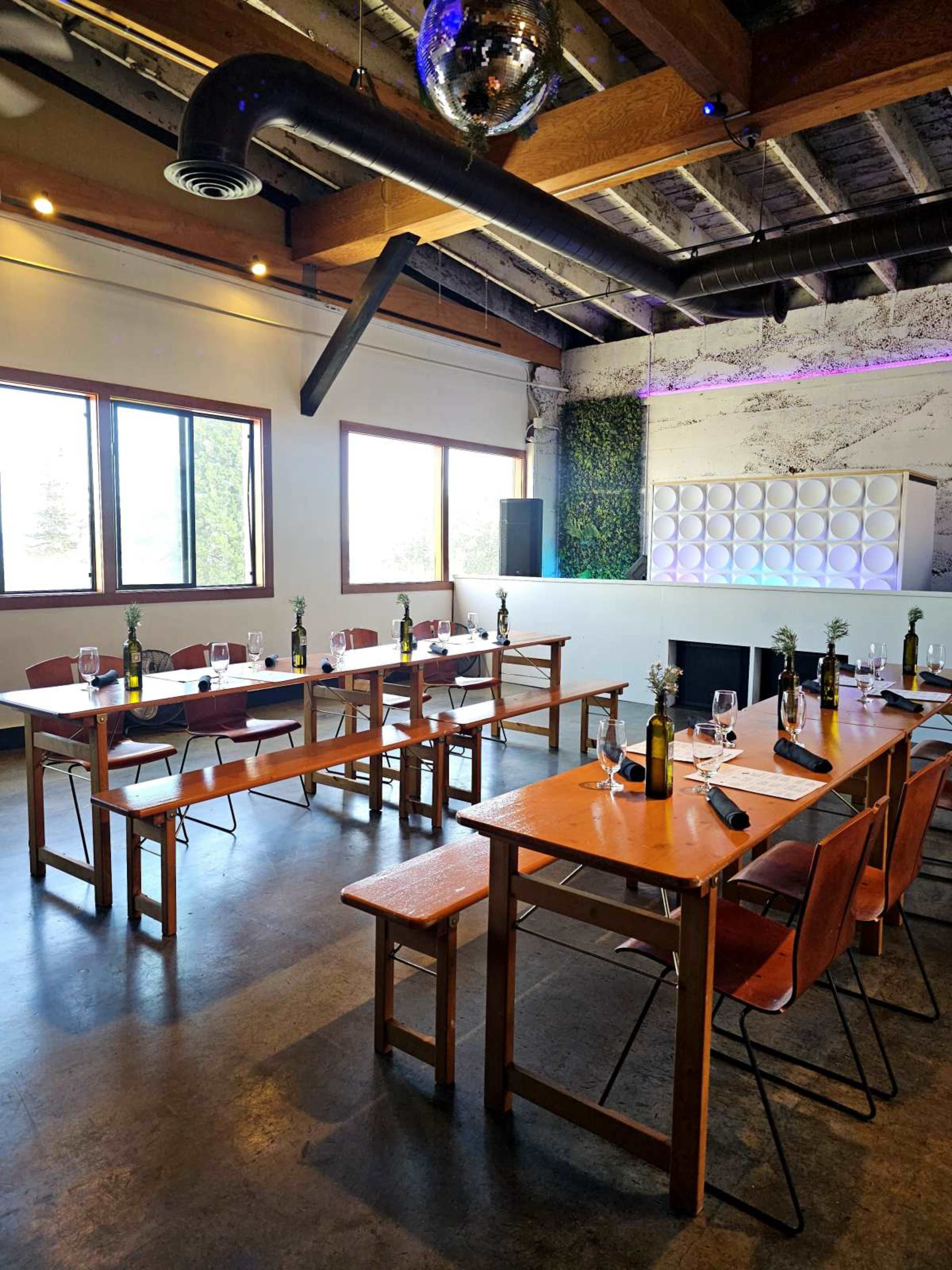 The image shows a modern dining space with wooden tables set for a meal, featuring wine bottles and glassware, under a ceiling with exposed beams and a disco ball.
