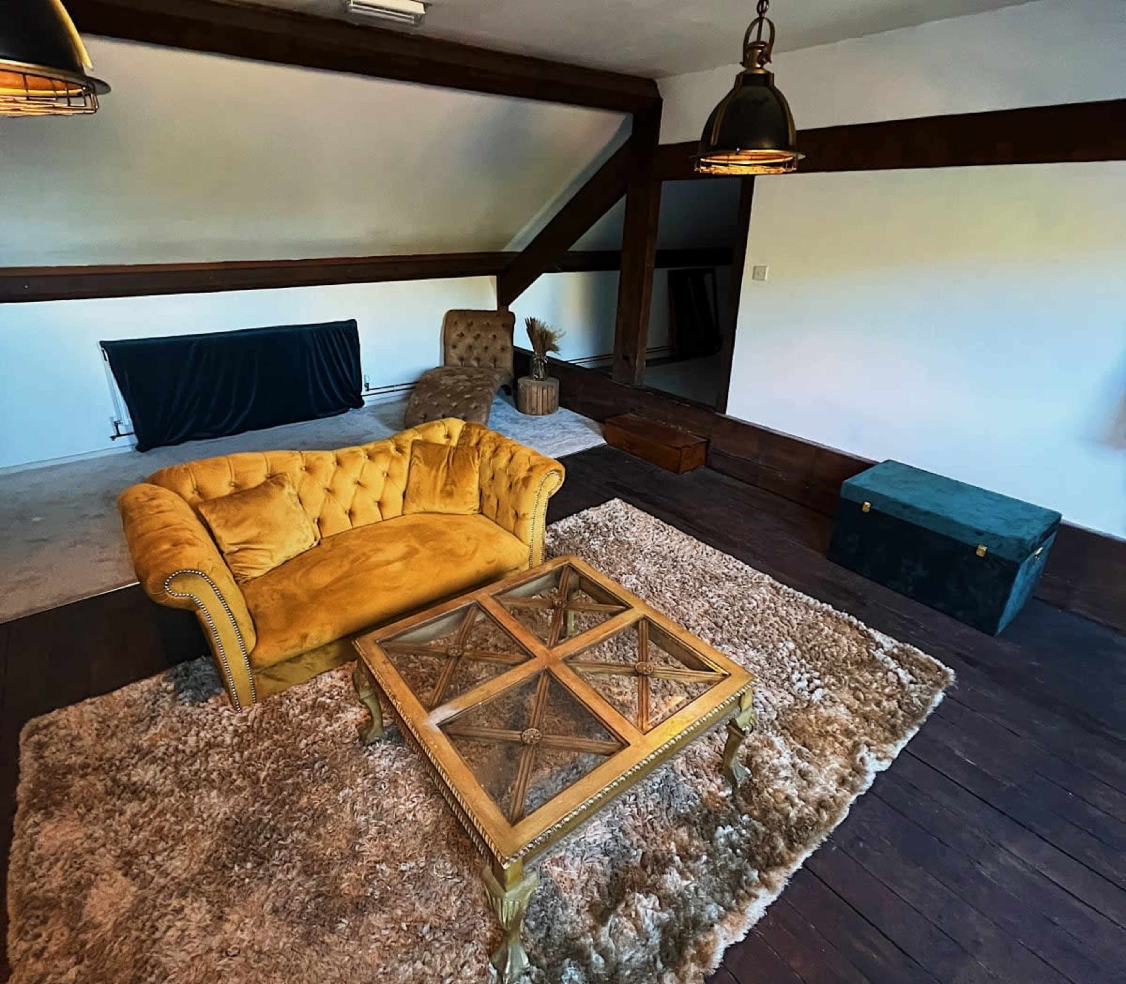 A cozy interior space with a yellow tufted sofa, a wooden coffee table with a geometric design, and a large area rug on a dark wooden floor.