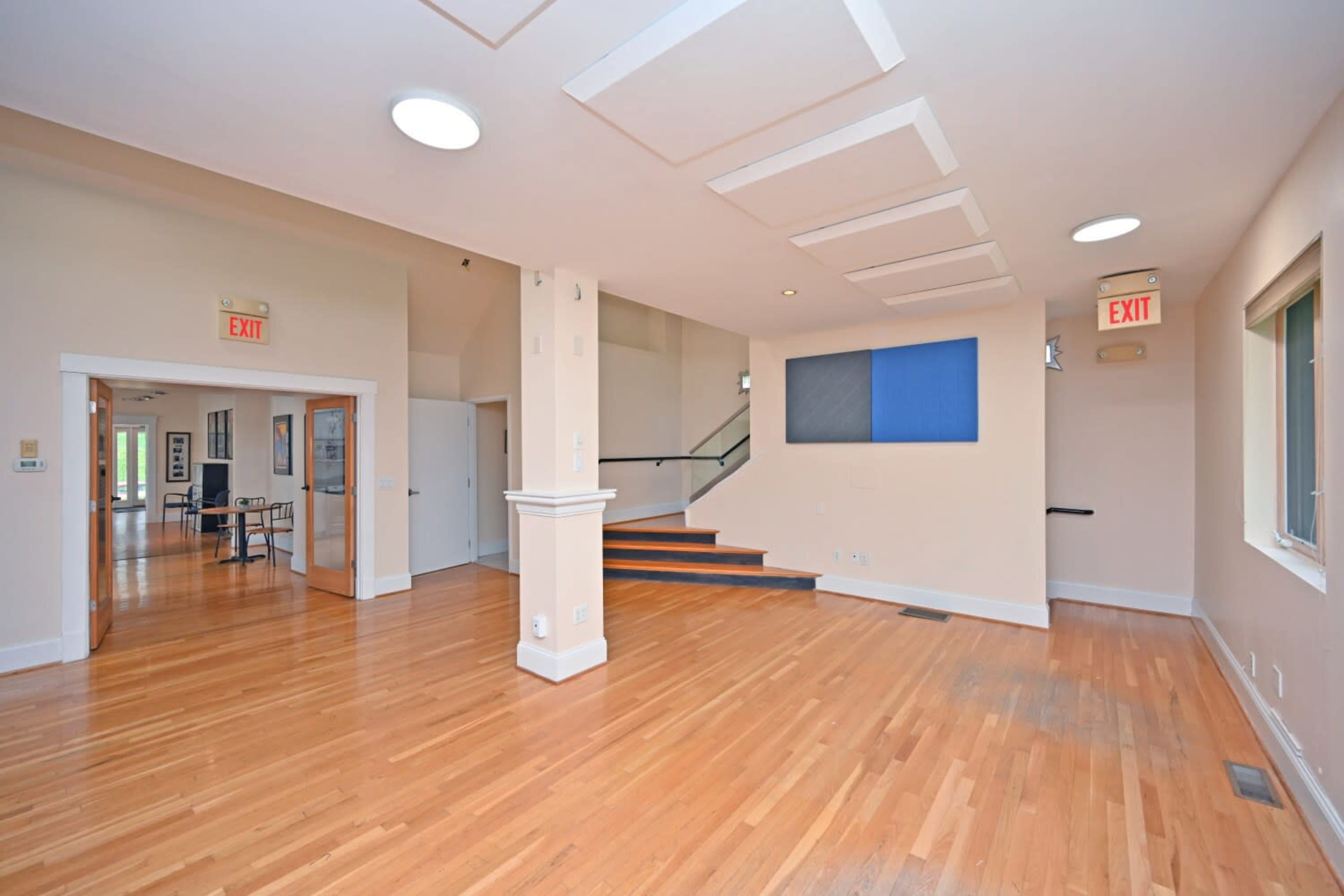 The image shows a spacious interior room with hardwood floors, high ceilings, and a staircase leading to an upper level.