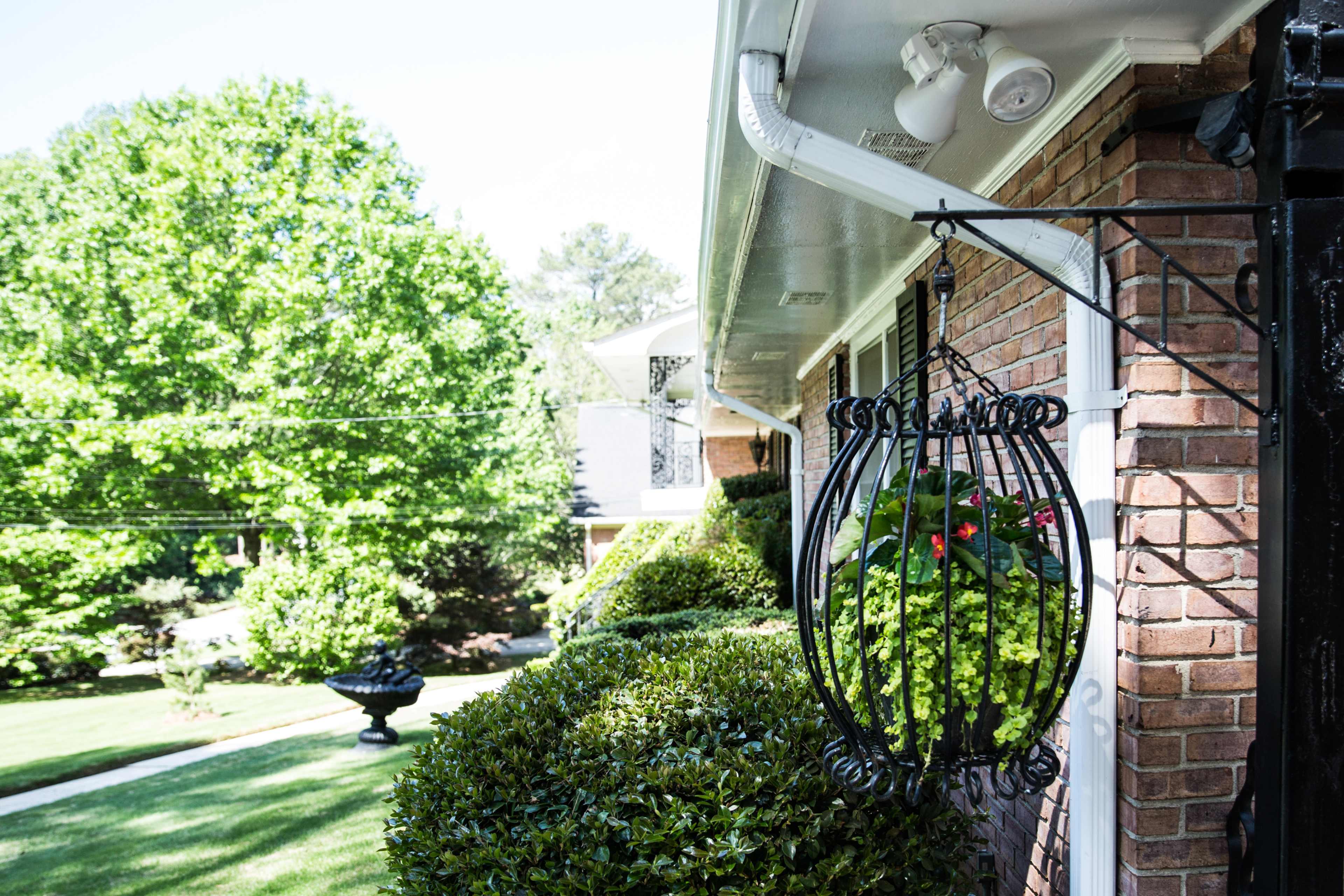 A hanging planter with greenery is mounted on a brick wall, overlooking a manicured lawn and trees.