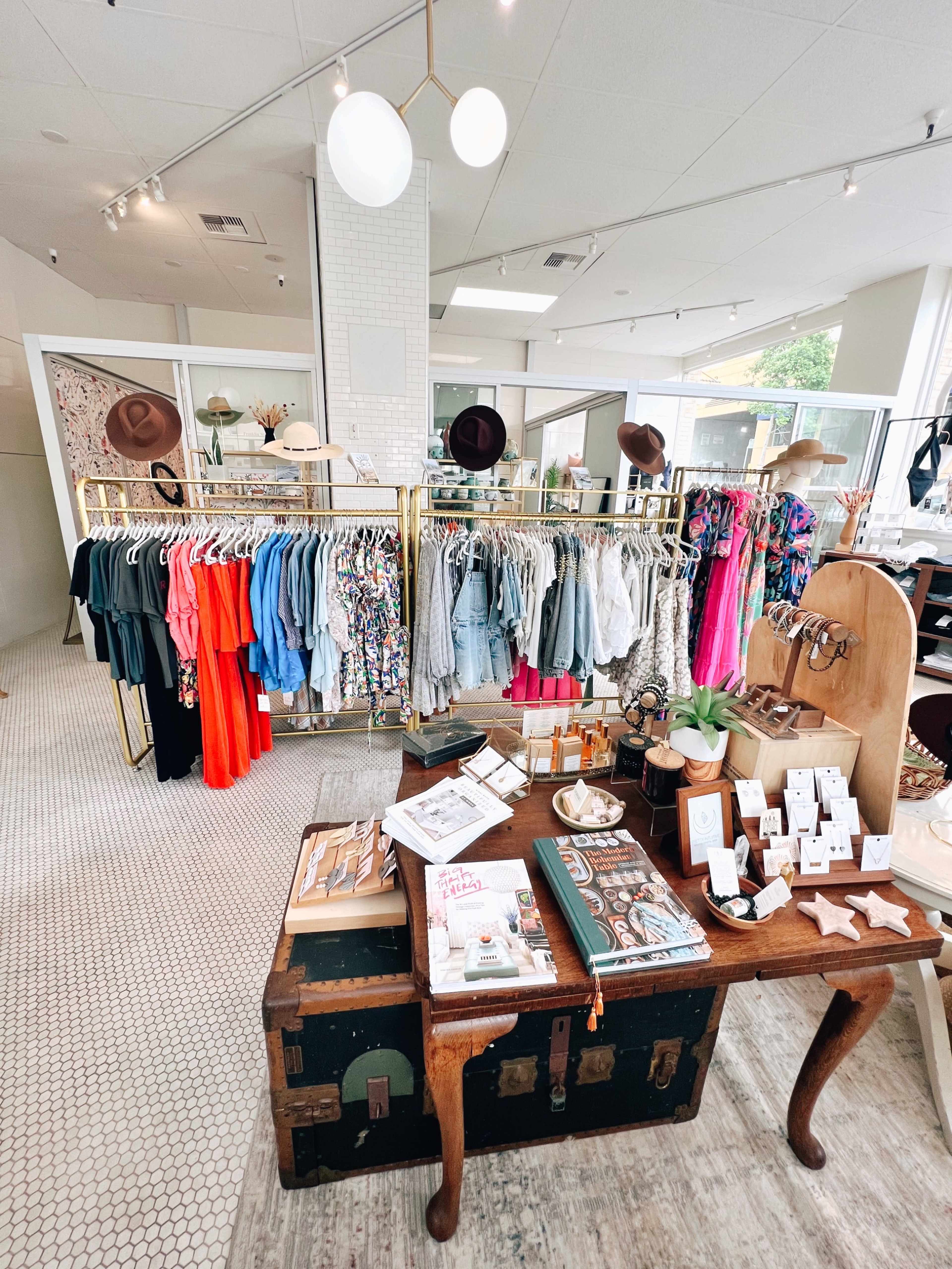 A clothing boutique featuring racks of women's apparel, a display table with accessories, and a bright, open layout.