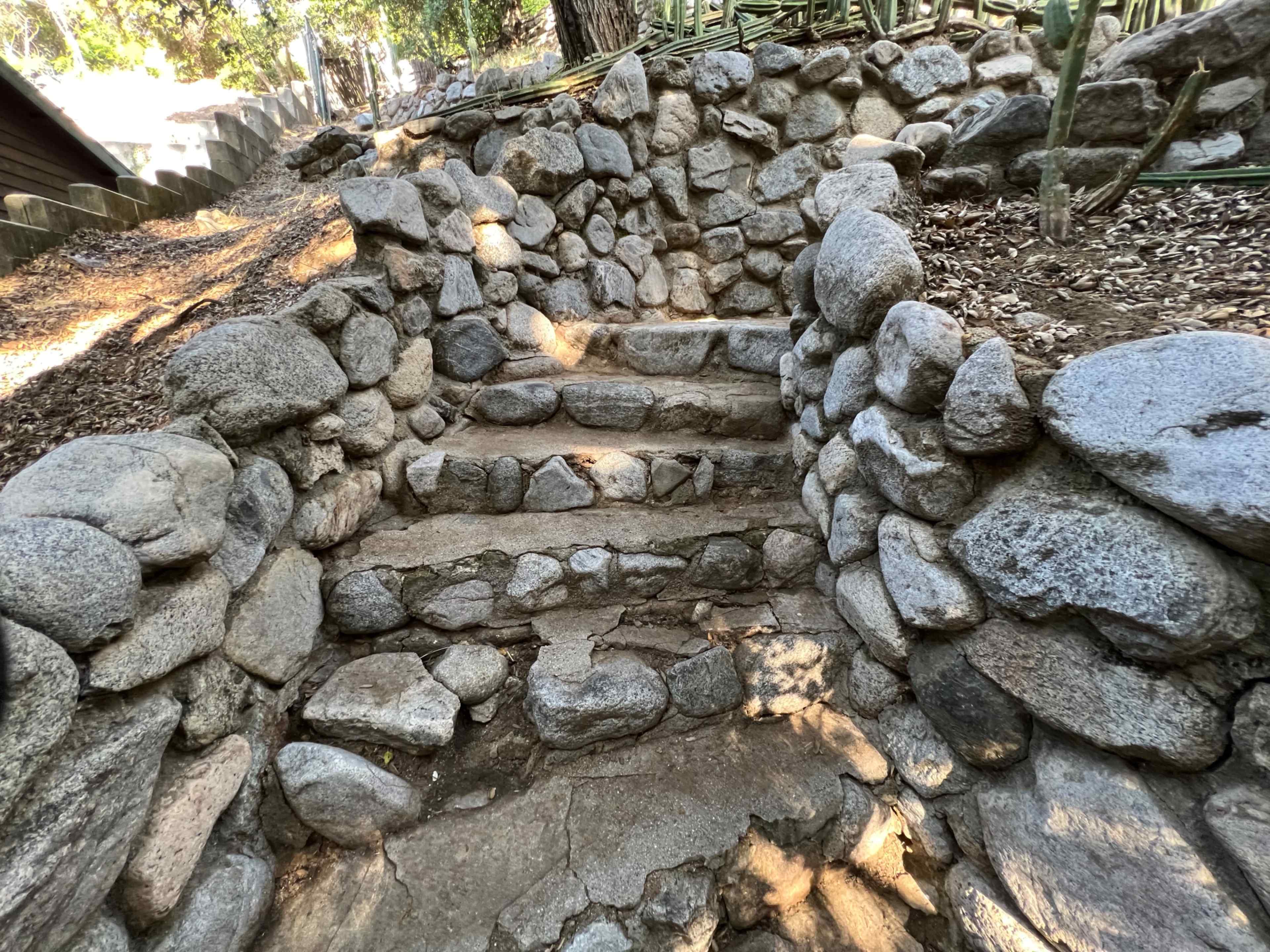 A series of stone steps leading up a pathway, bordered by rocky walls and surrounded by greenery.