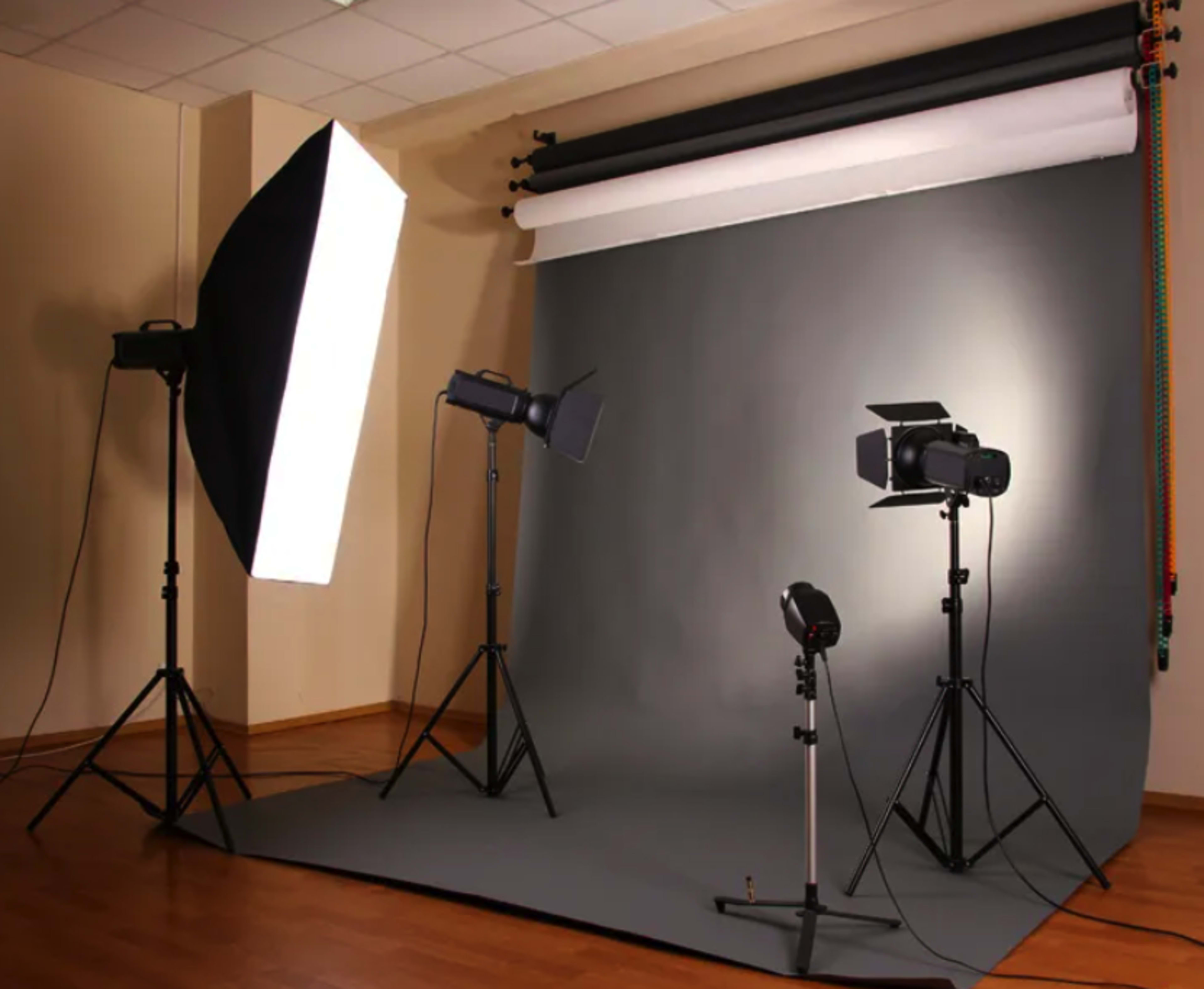A photography studio setup with multiple lights positioned around a gray backdrop on a wooden floor.