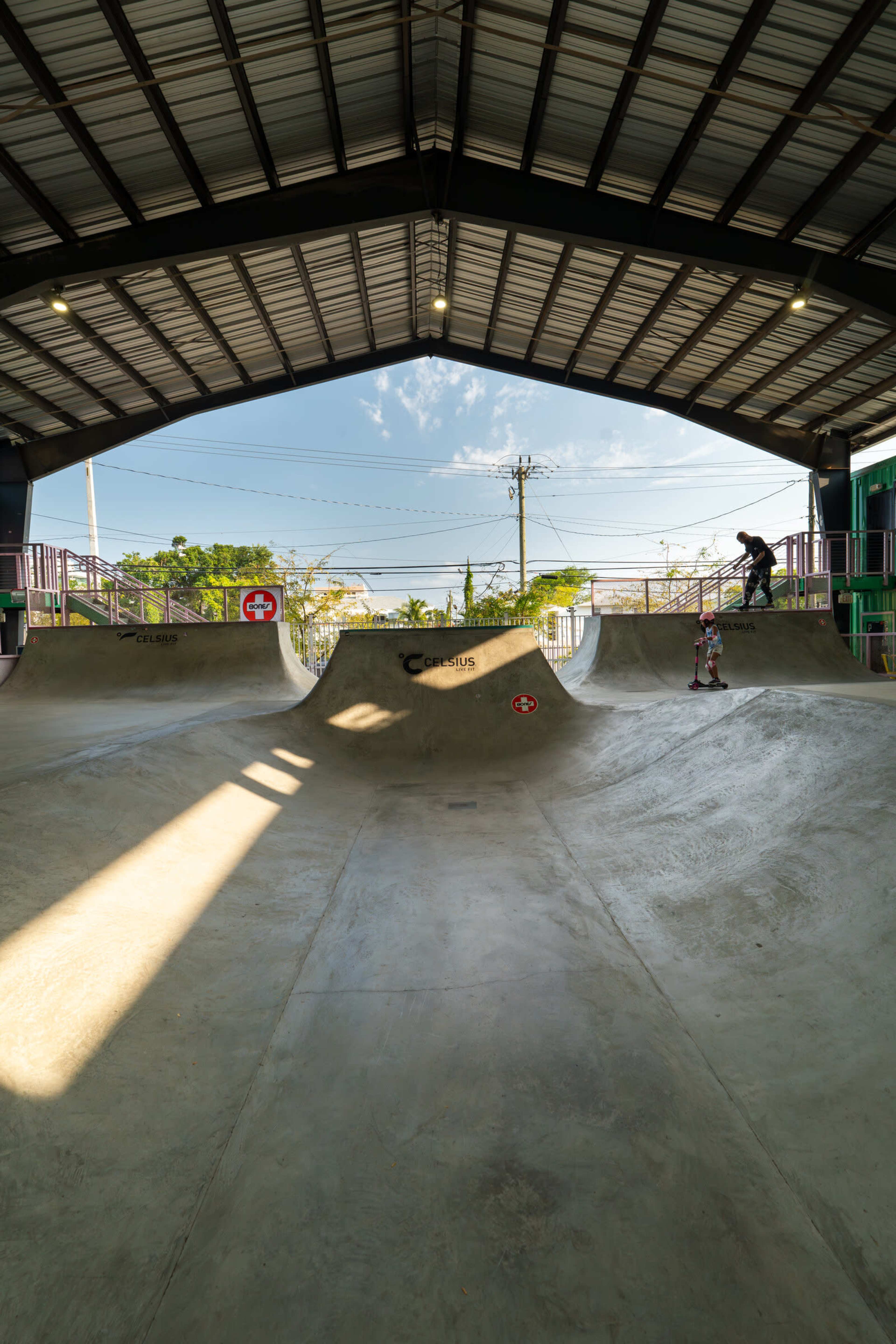 The image shows a skatepark indoors with curved concrete ramps and a skater preparing to ride.