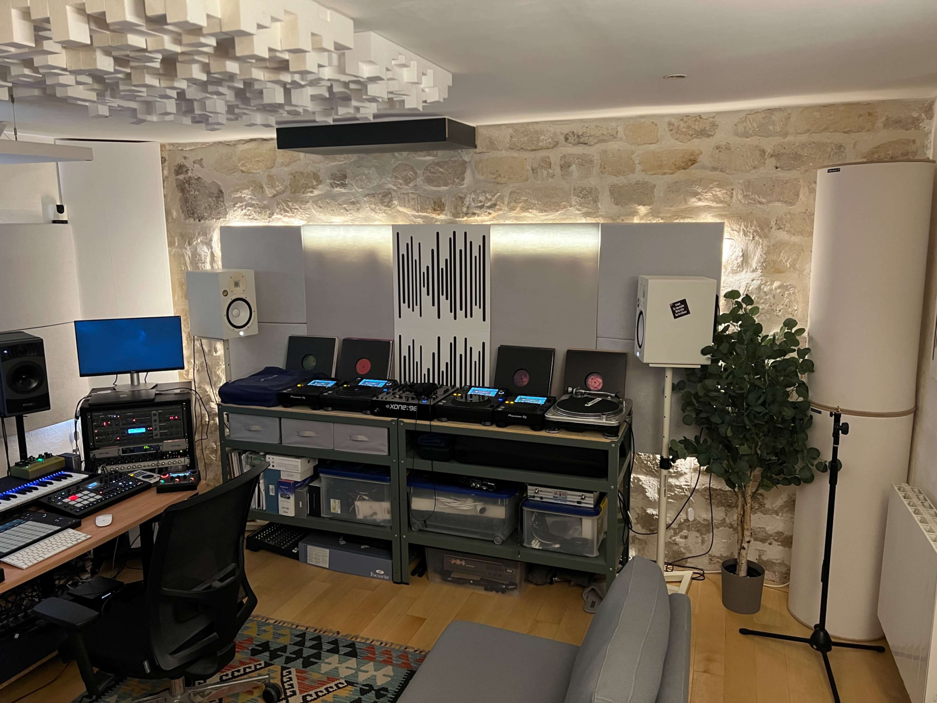 A music studio features audio equipment, mixing consoles, and speakers, with a stone wall and ambient lighting.