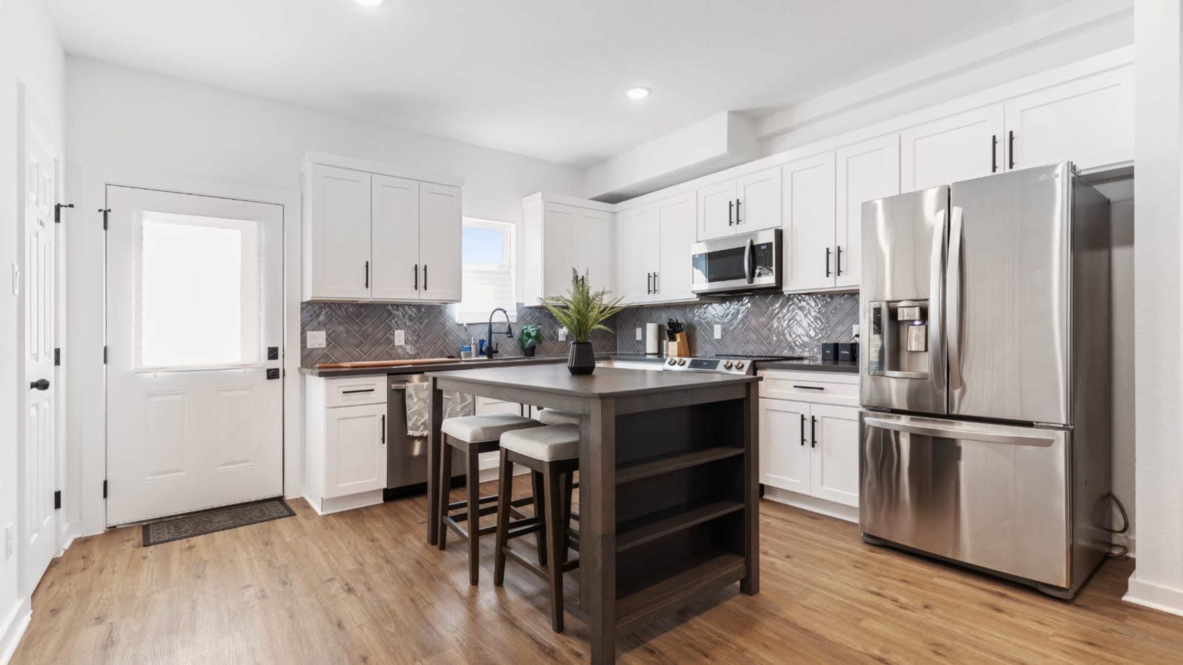 A modern kitchen features white cabinets, stainless steel appliances, and a central island with seating.
