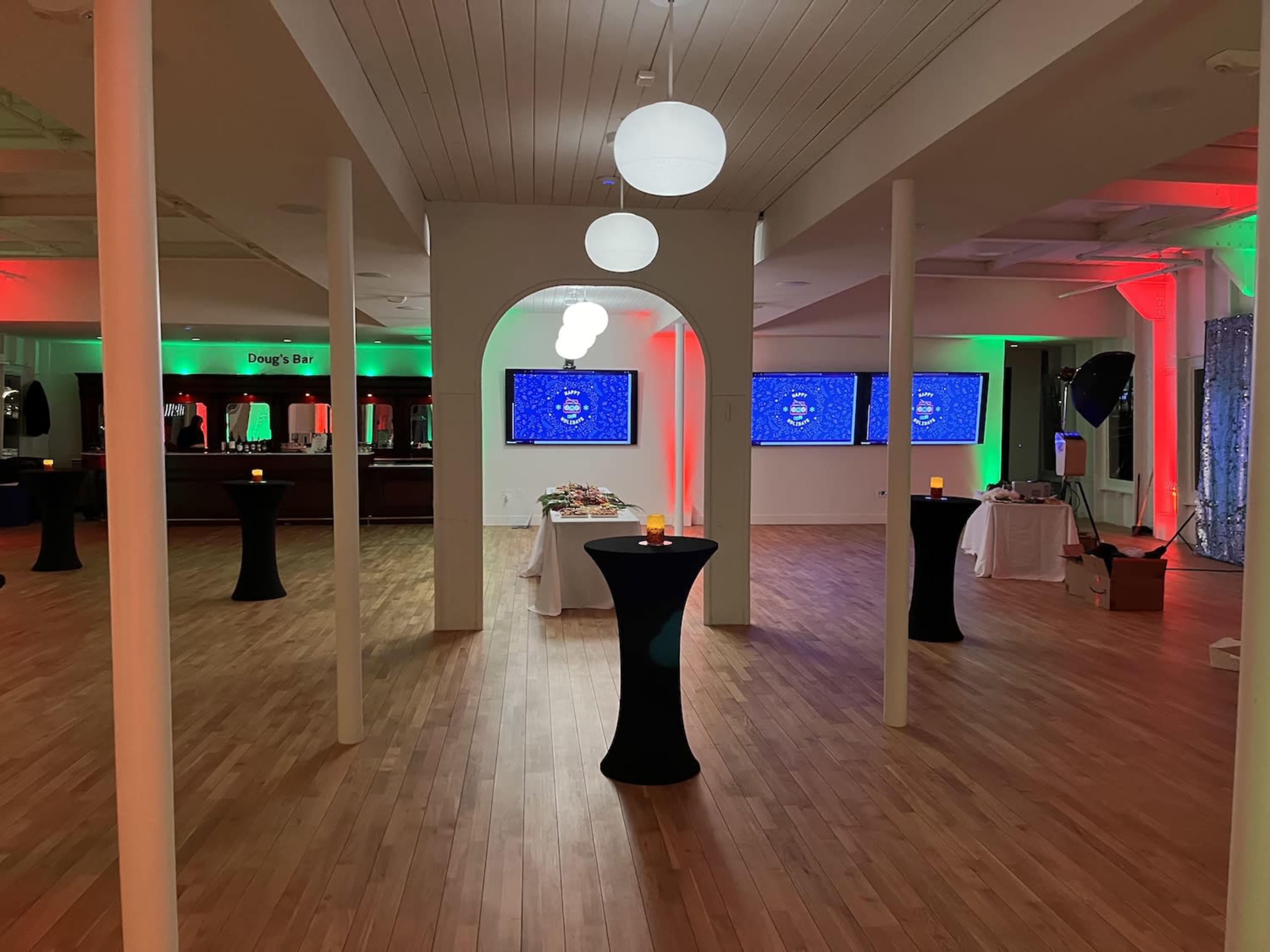 The image shows a spacious event room with low tables, screens displaying visuals, and ambient lighting in red and green.