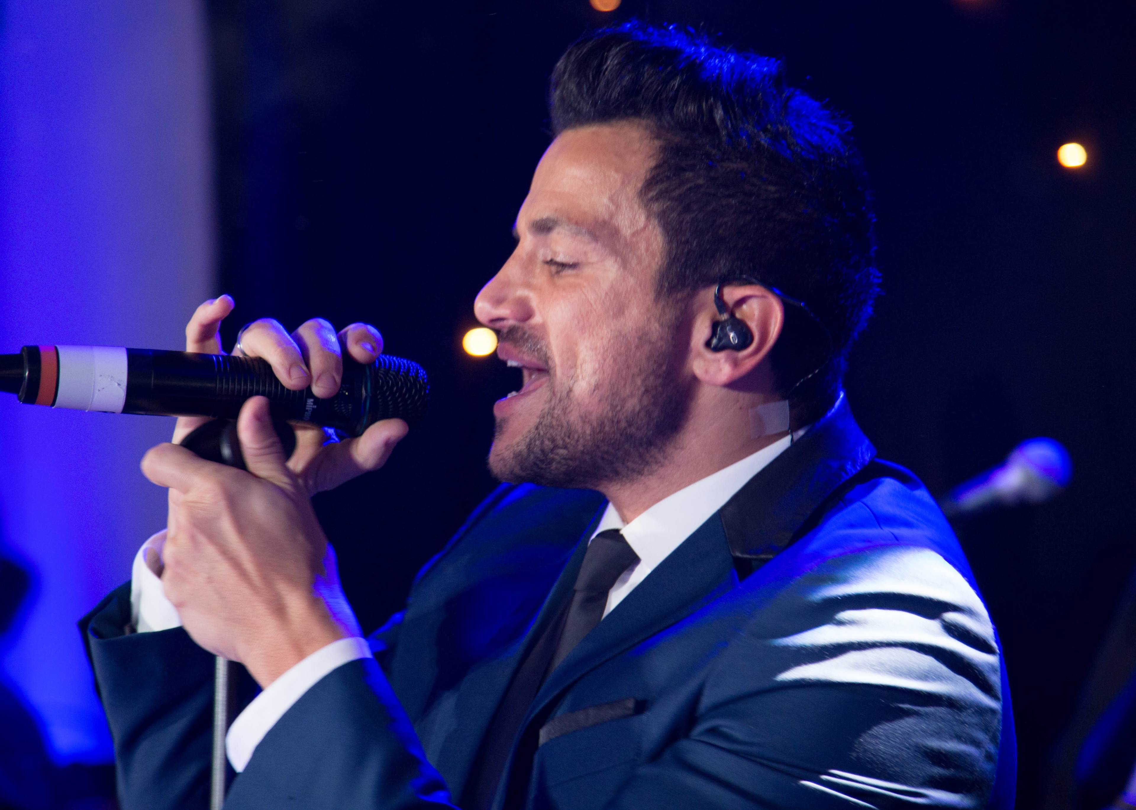 A man in a blue suit sings into a microphone on stage.