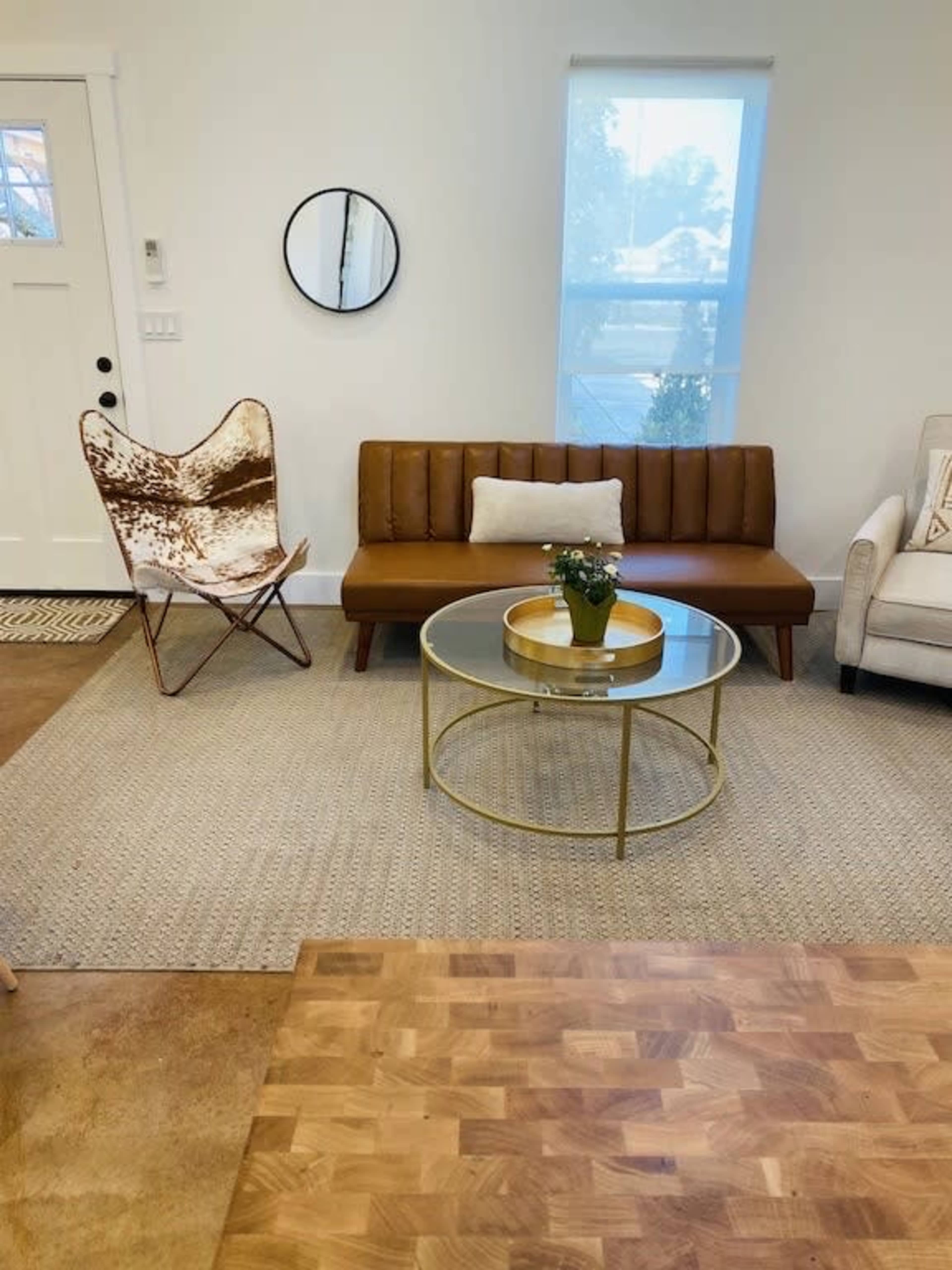 A modern living room with a brown leather sofa, a round glass coffee table, a butterfly chair, and a small plant on the table.