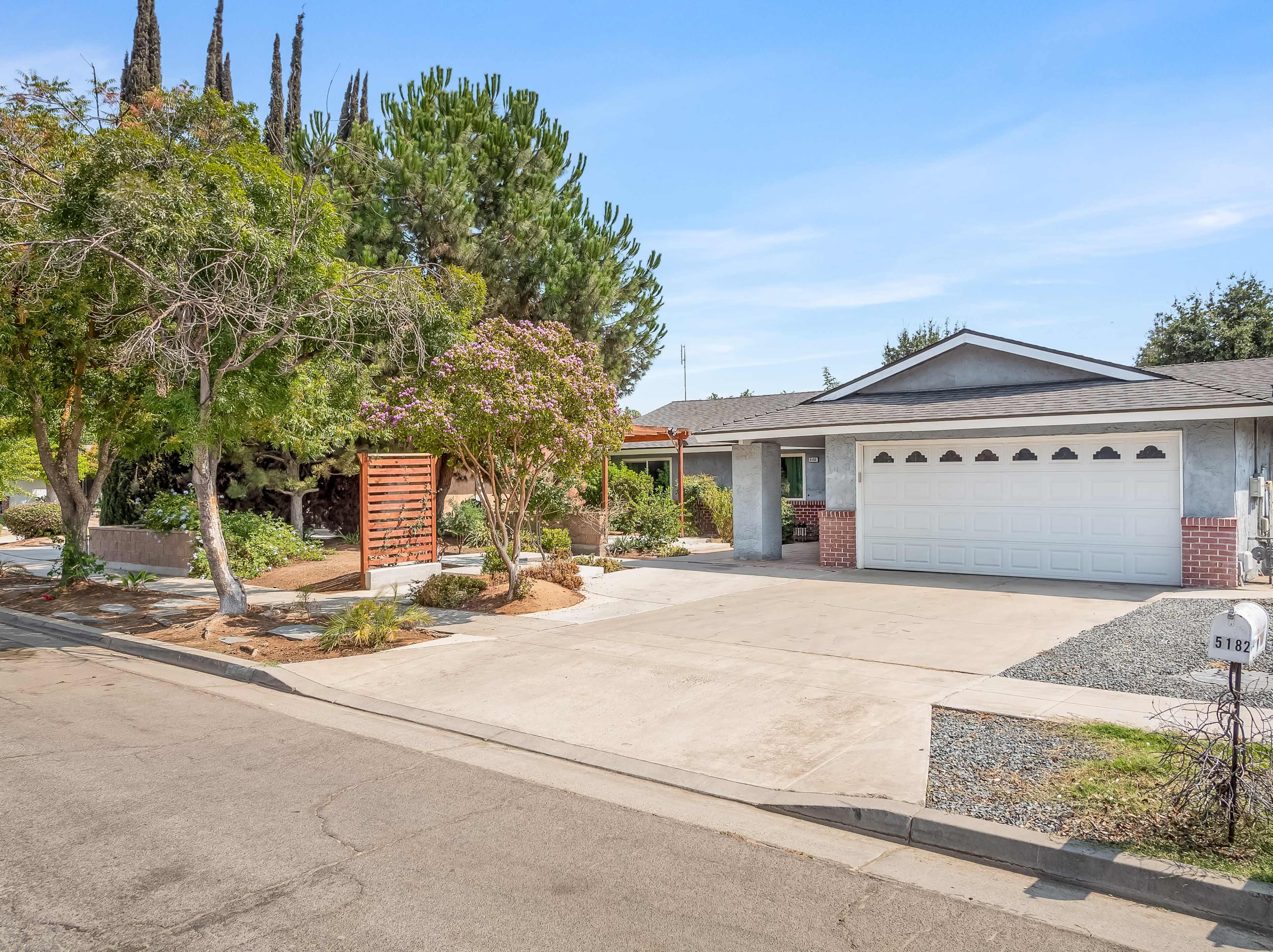 A suburban house with a gray exterior, a two-car garage, and landscaped front yard along a quiet street.