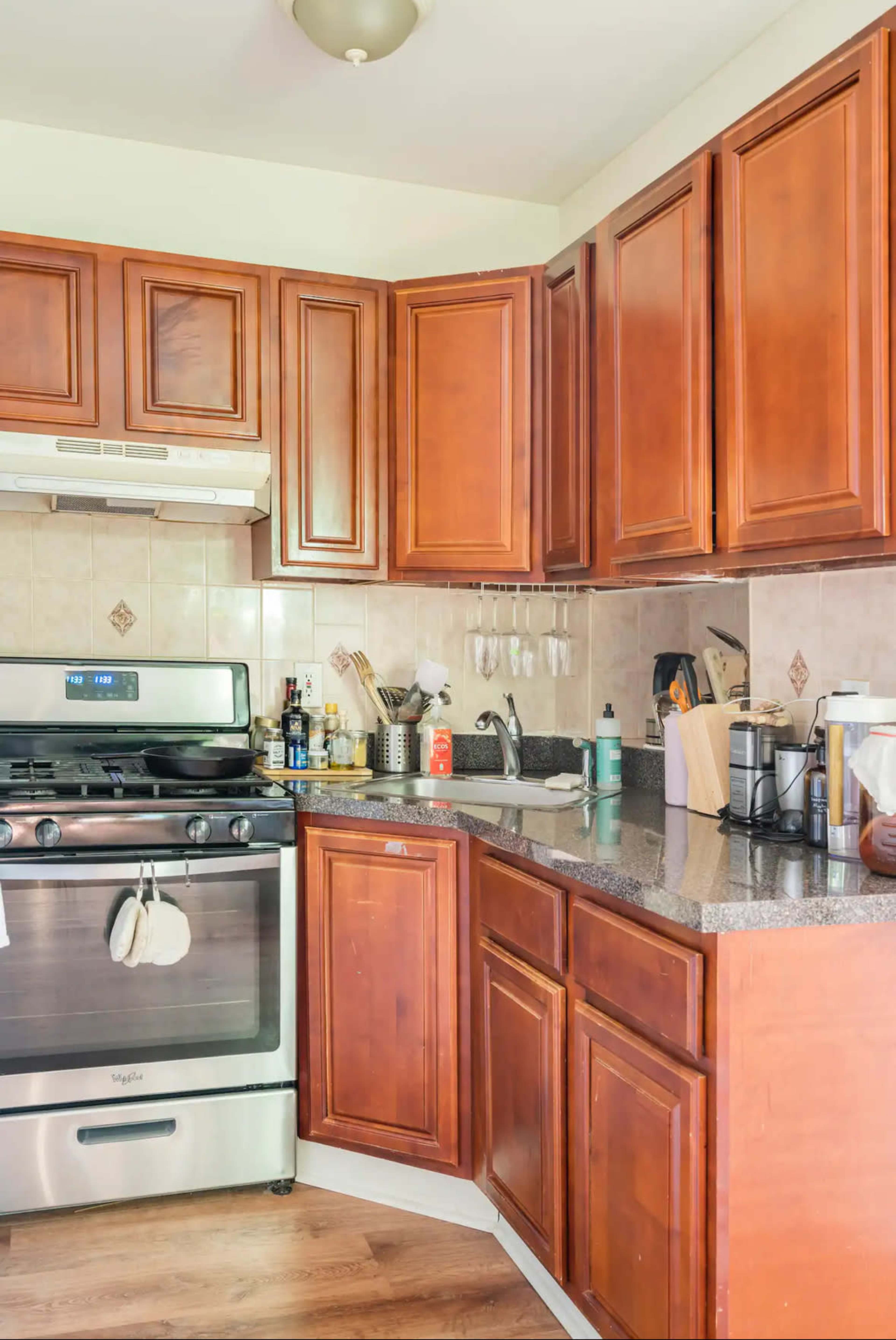 The image shows a kitchen with wooden cabinets, a stainless steel gas stove, and a granite countertop.