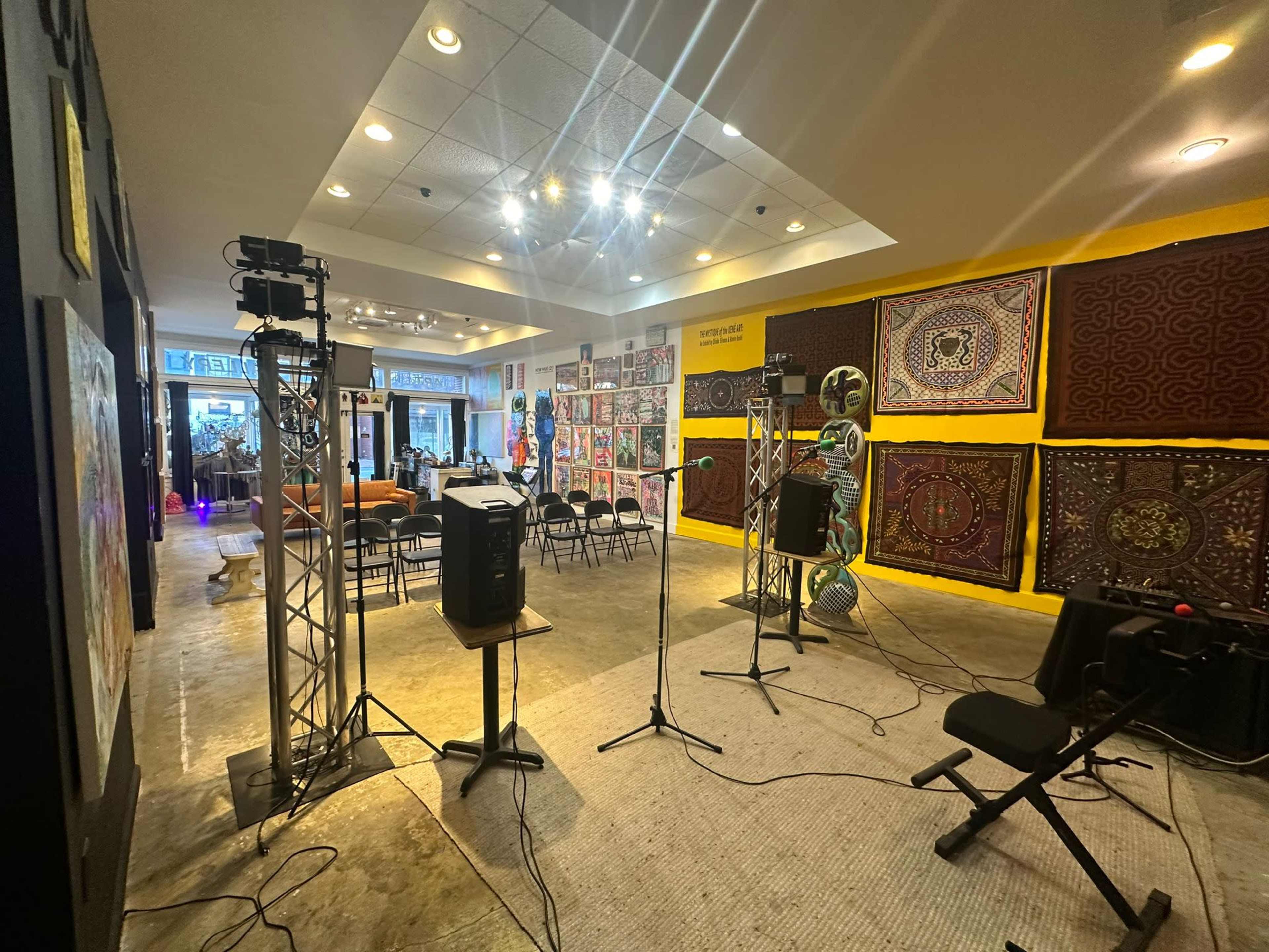 The image shows a spacious gallery or exhibition area with colorful wall hangings and equipment set up for a performance or presentation.