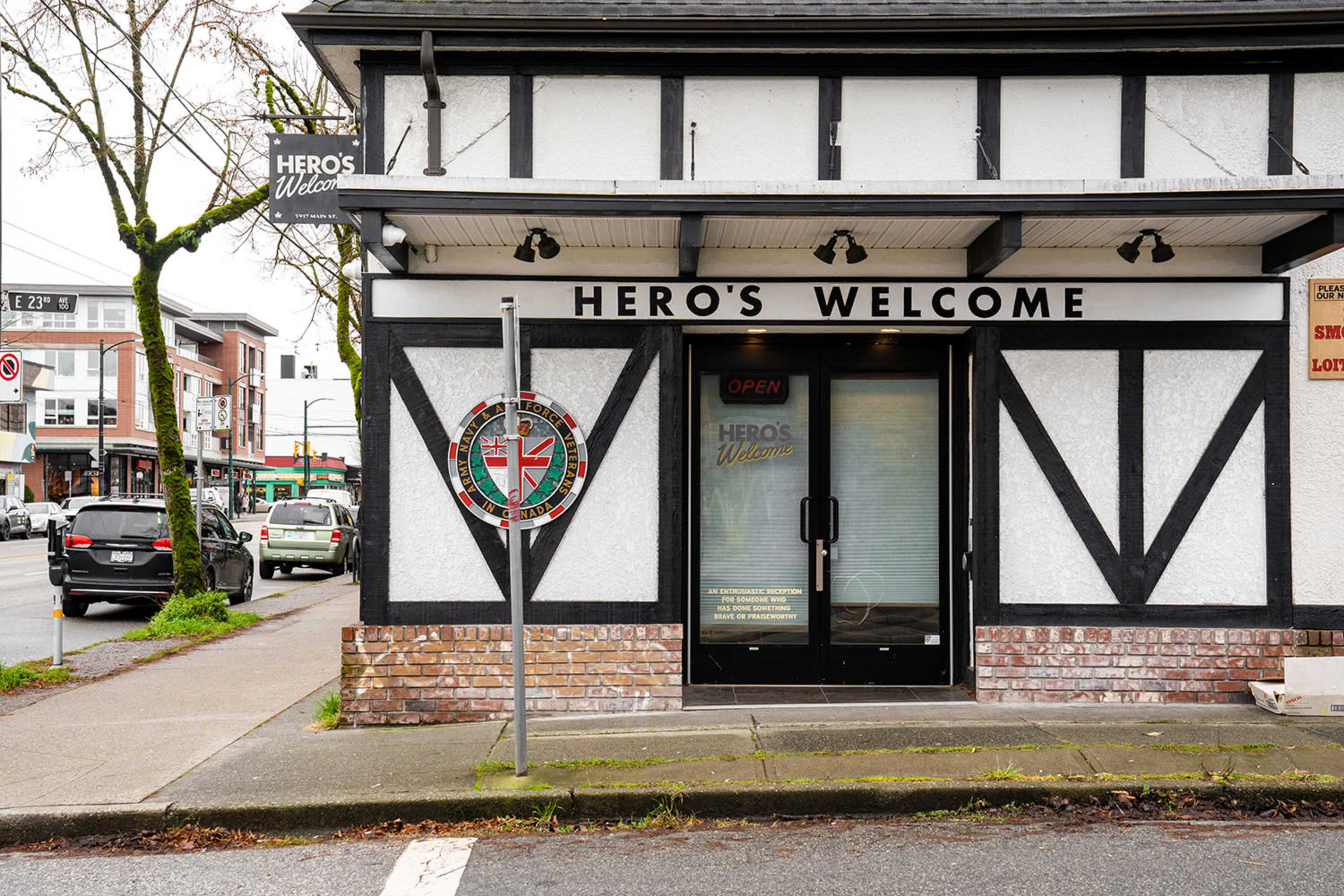 The image shows a storefront with the sign "Hero's Welcome" displayed above the entrance, featuring a badge emblem to the side and a clear glass door.