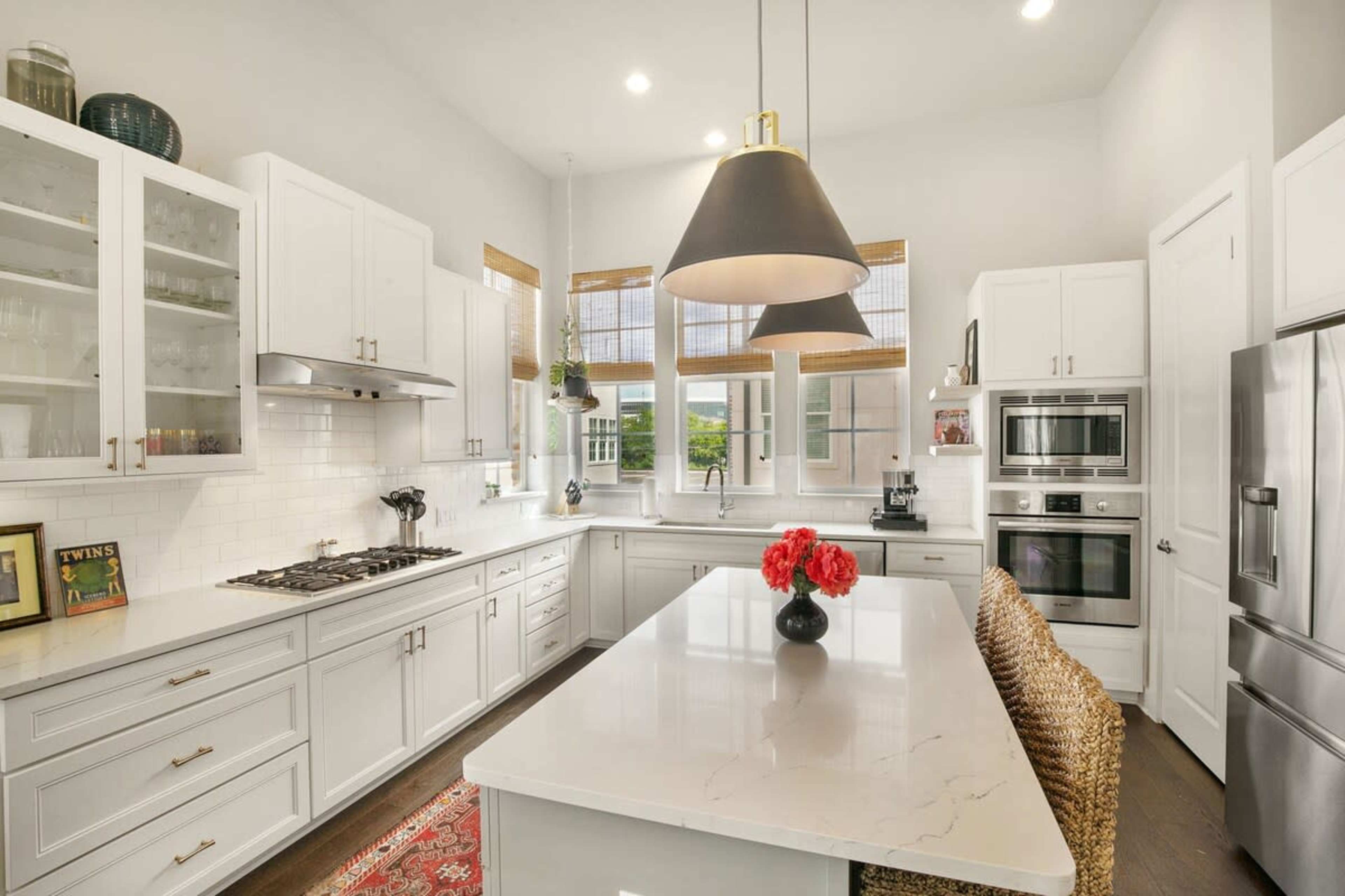 The image features a modern kitchen with white cabinetry, stainless steel appliances, and a large island topped with a marble surface and a vase of red flowers.