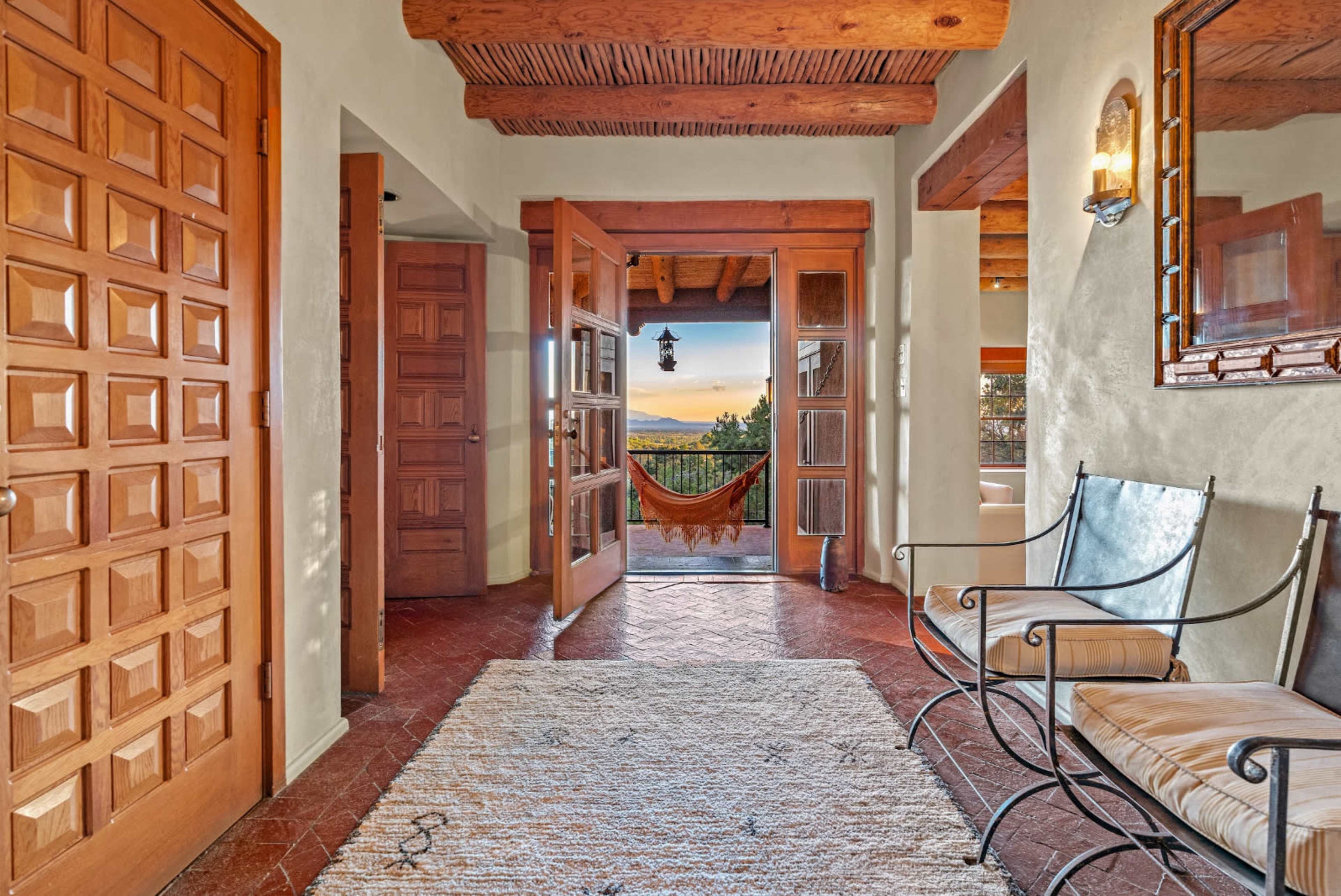 A spacious entrance hallway with wooden doors, a hammock hanging in an open doorway, and a rug on the tiled floor.