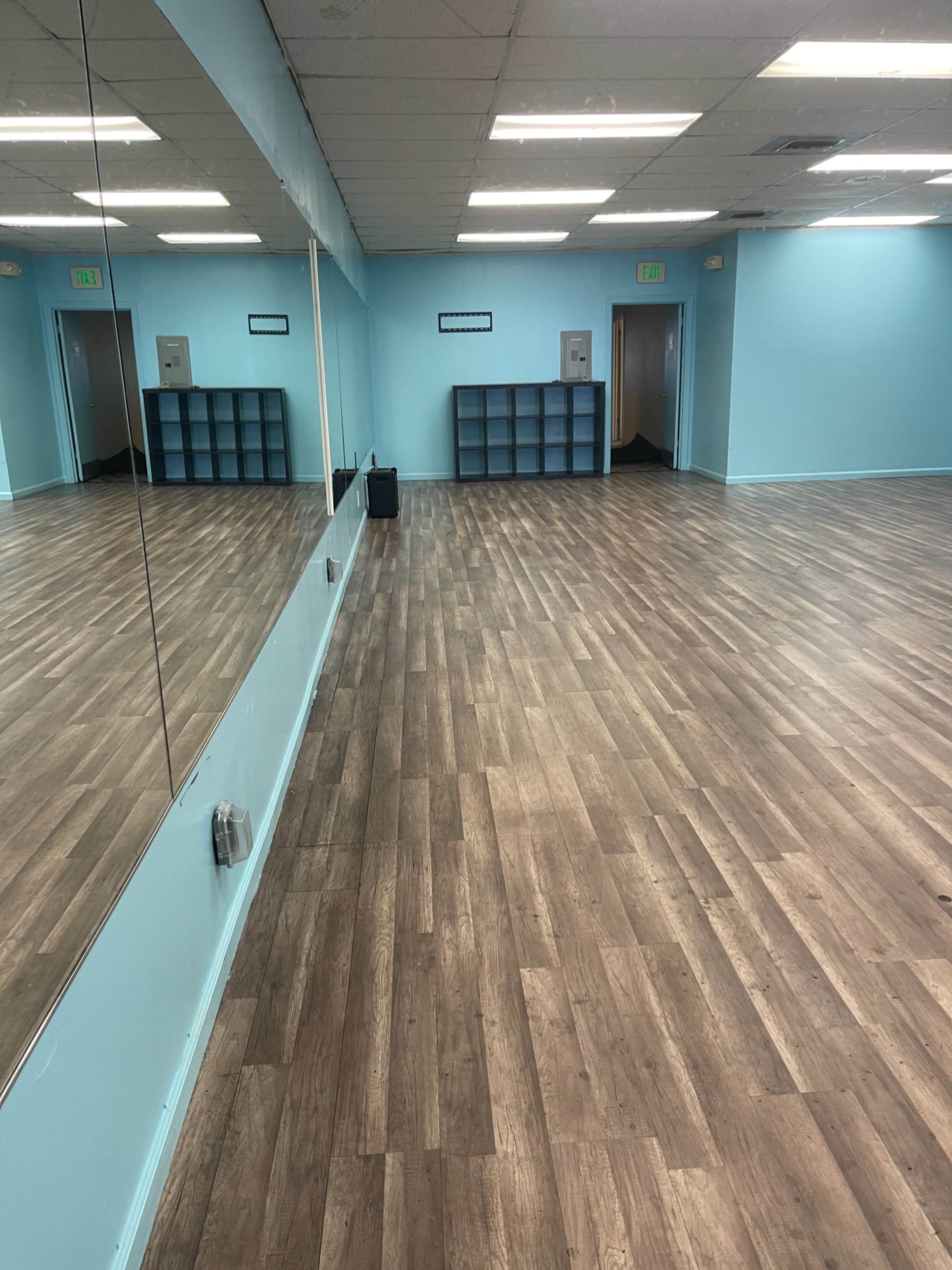 A spacious room with wooden flooring, light blue walls, and a large mirror along one side.