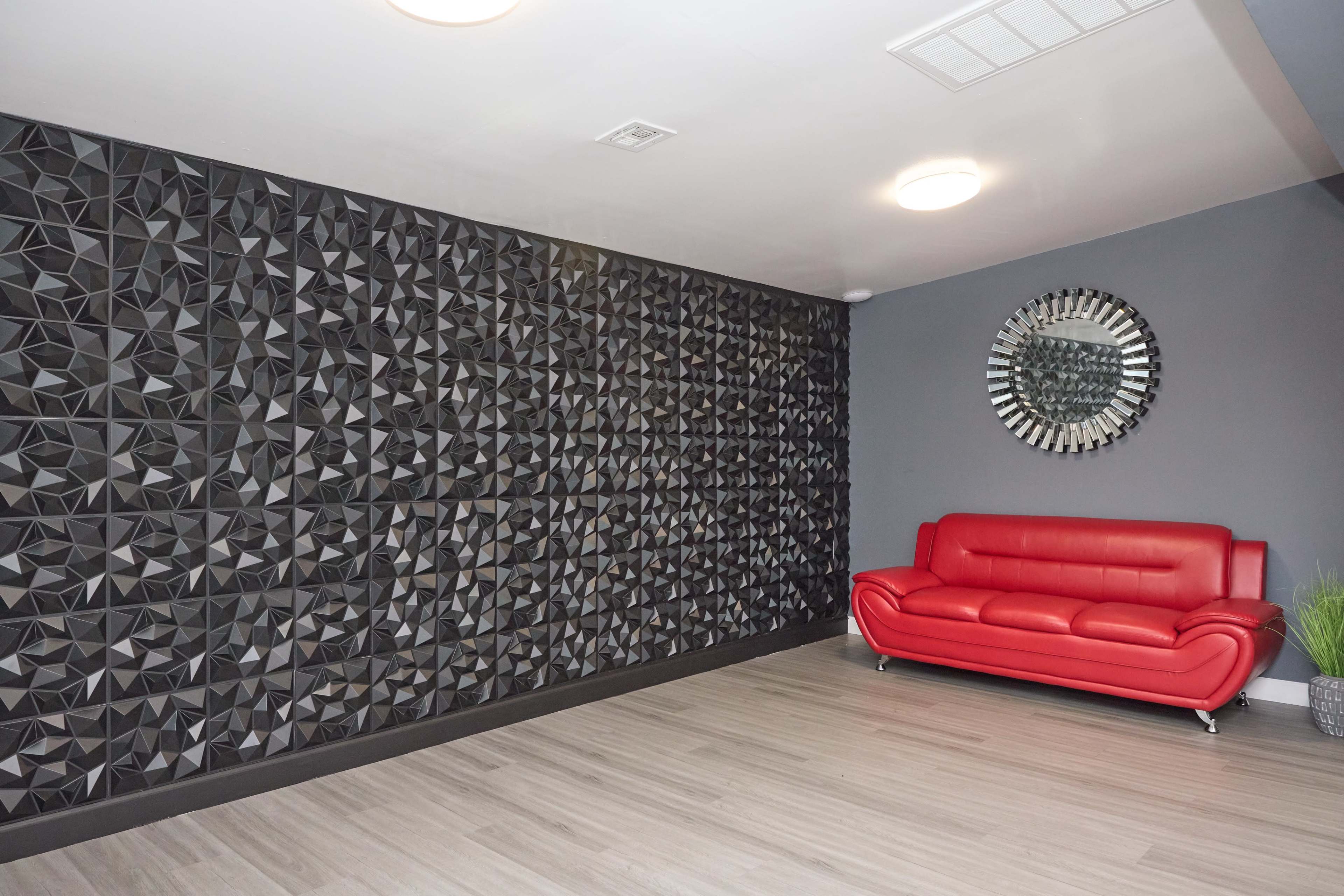 The image shows a modern interior with a textured black wall, a red leather couch, a round mirror, and light-colored flooring.